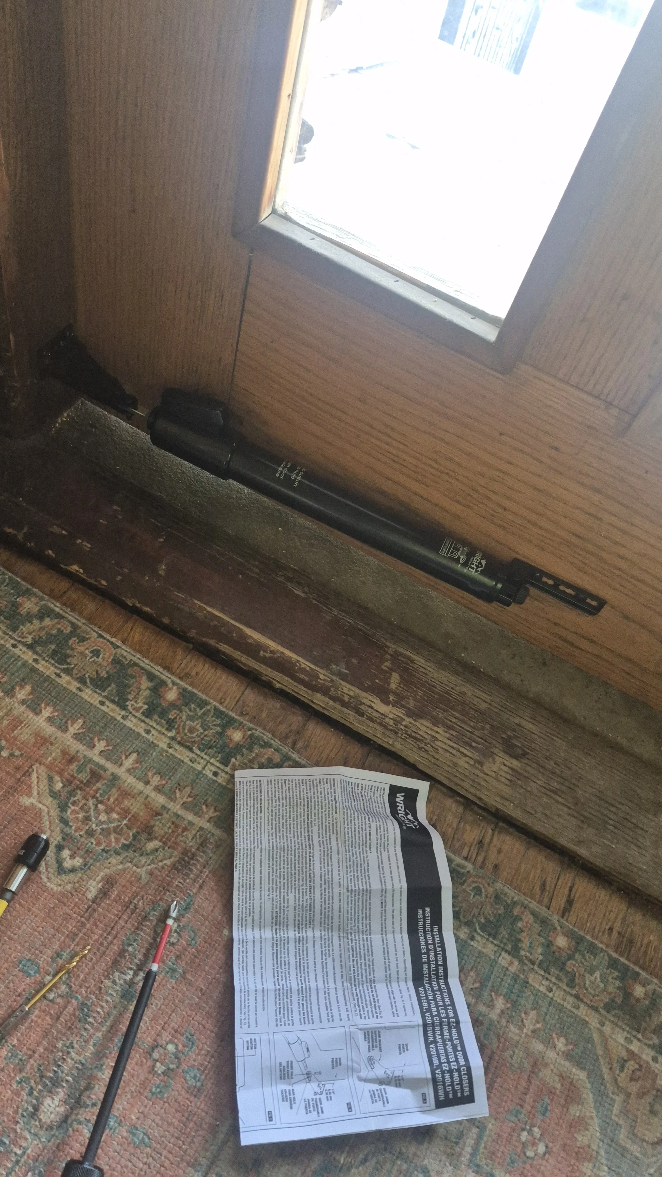 Tools, a user manual, and a metal pole lying on a patterned carpet next to a wooden door with a window; Washington Park, Denver, Colorado