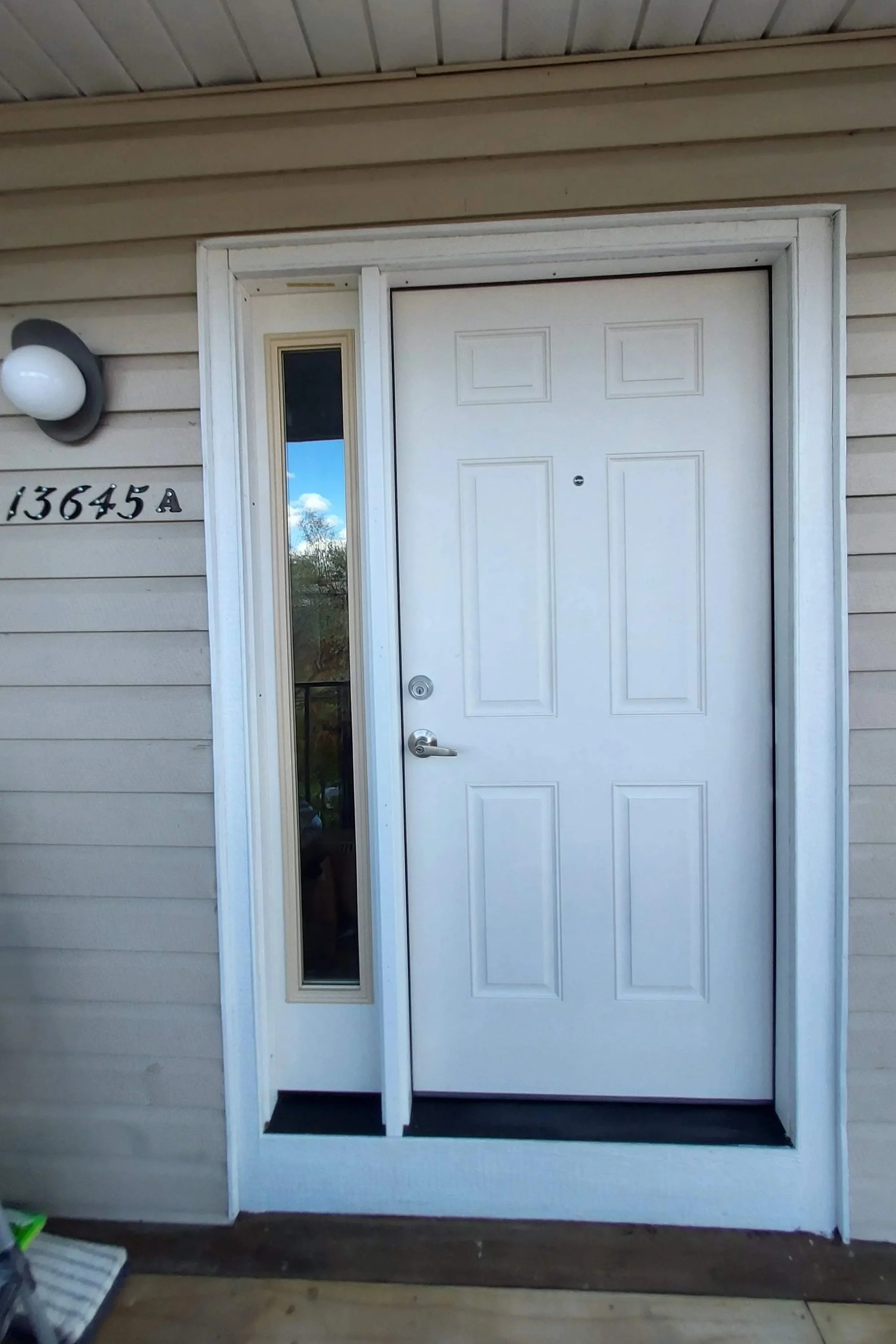 Front view of a house entrance featuring a white door with geometric panels, a side window, house number 13645A, and an exterior light fixture.