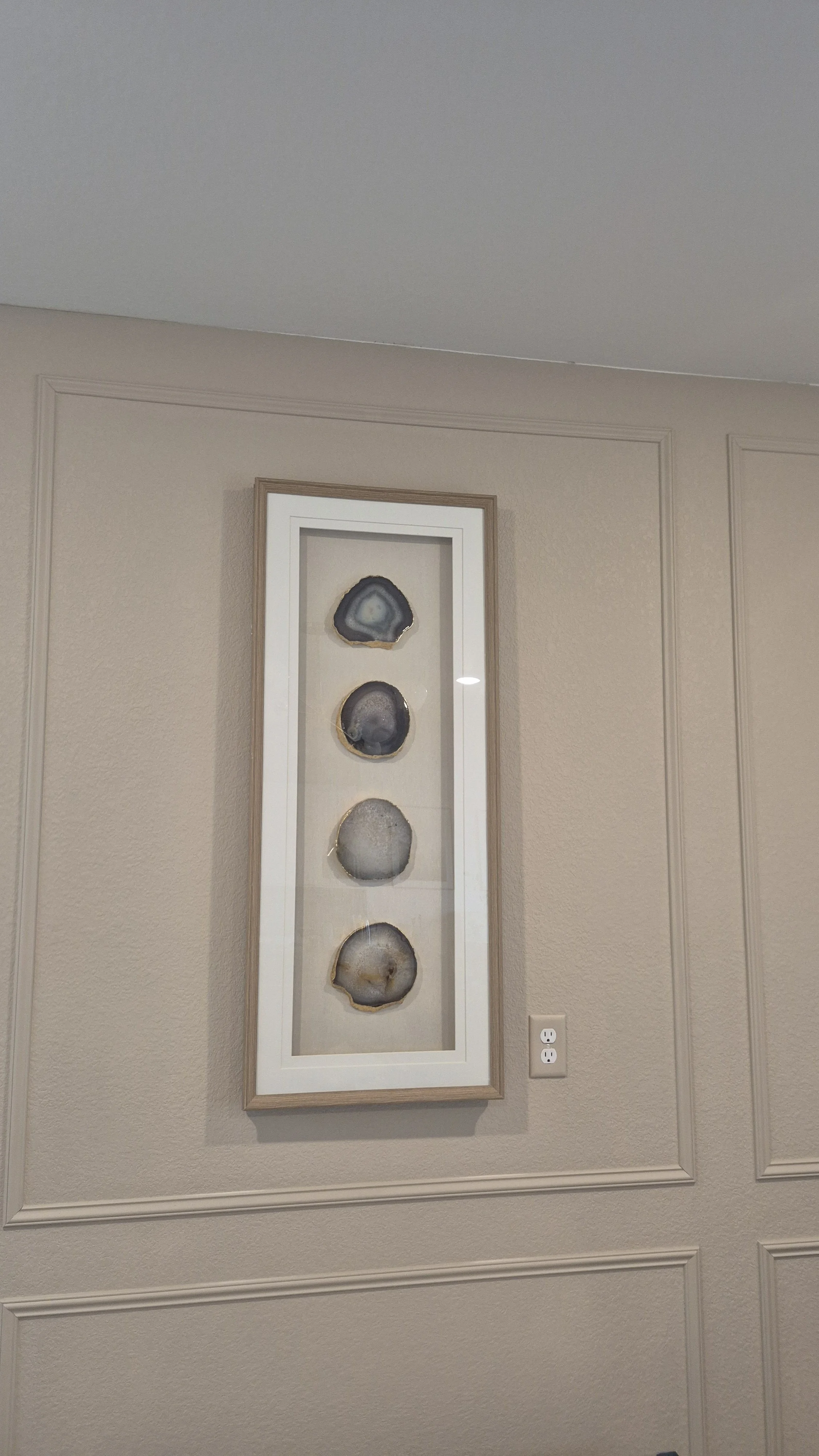 Framed artwork with four geode slices mounted vertically on a beige wall; Erie, Colorado