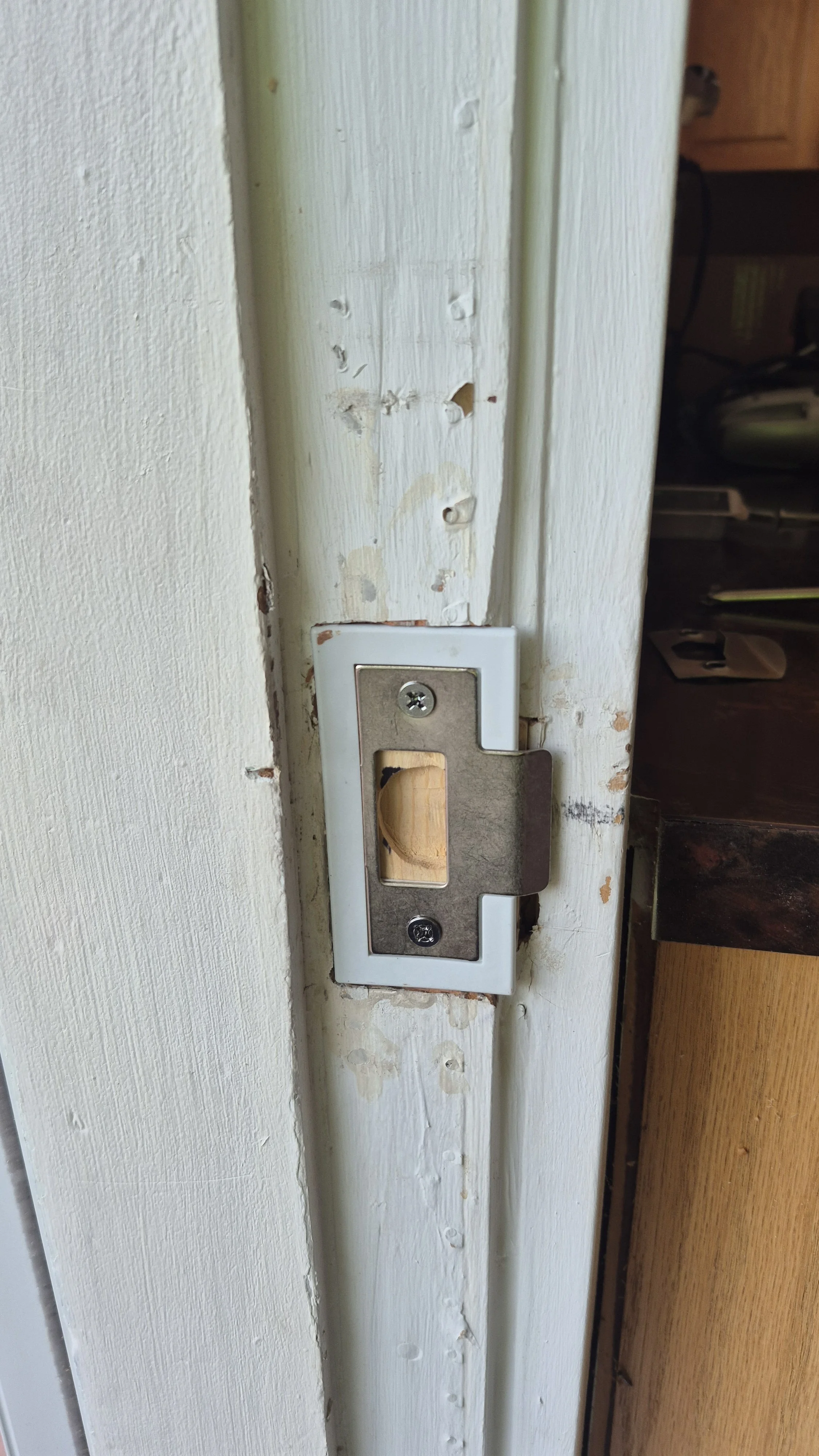 Close-up of a door latch plate missing the latch, with visible screws and chipping paint around the door frame; Wheat Ridge, Colorado