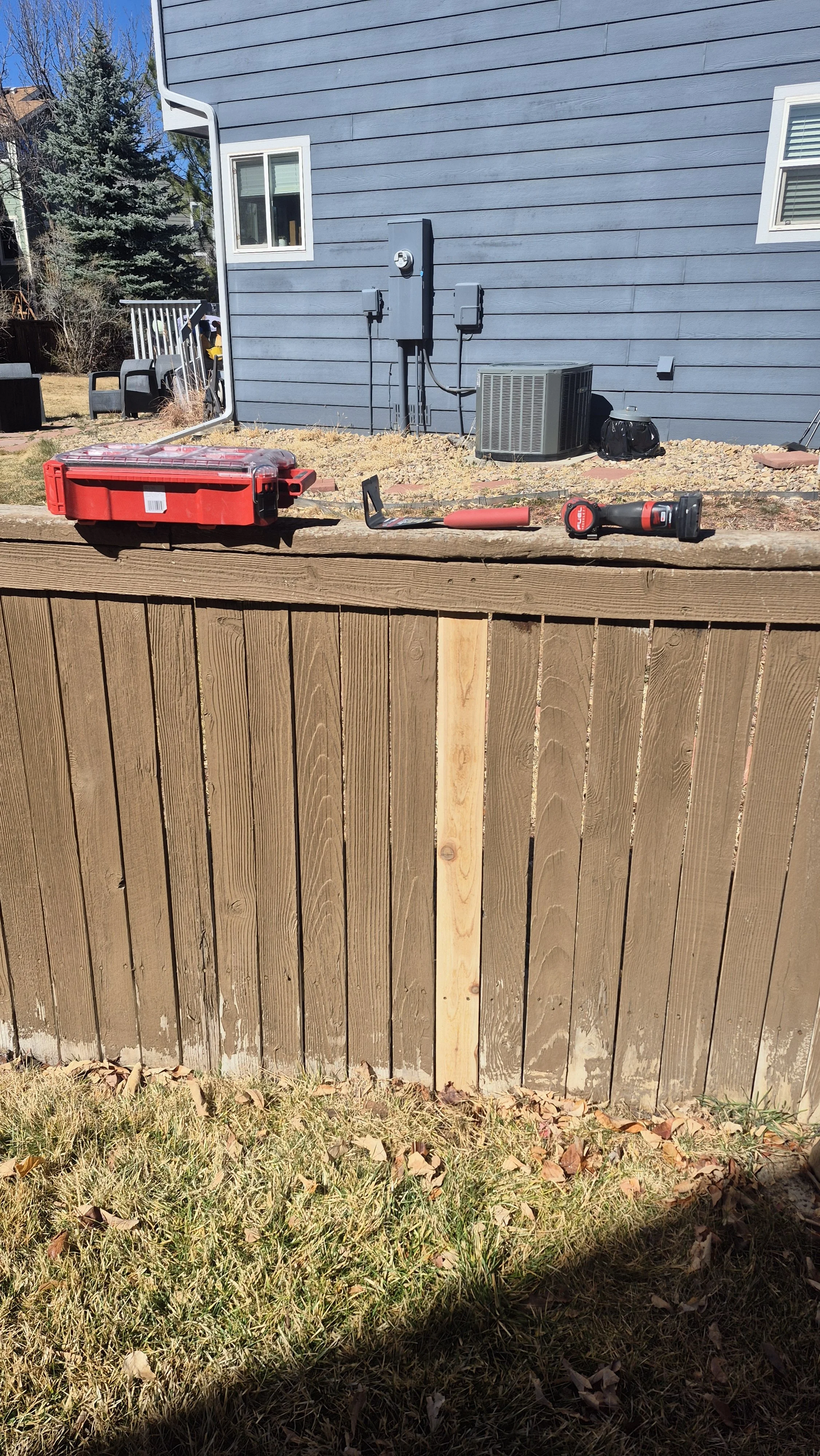 Outdoor scene showing a wooden fence, tools including a wrench and cordless drill, a red toolbox, and a house with blue siding in the background, Edgewater, Colorado