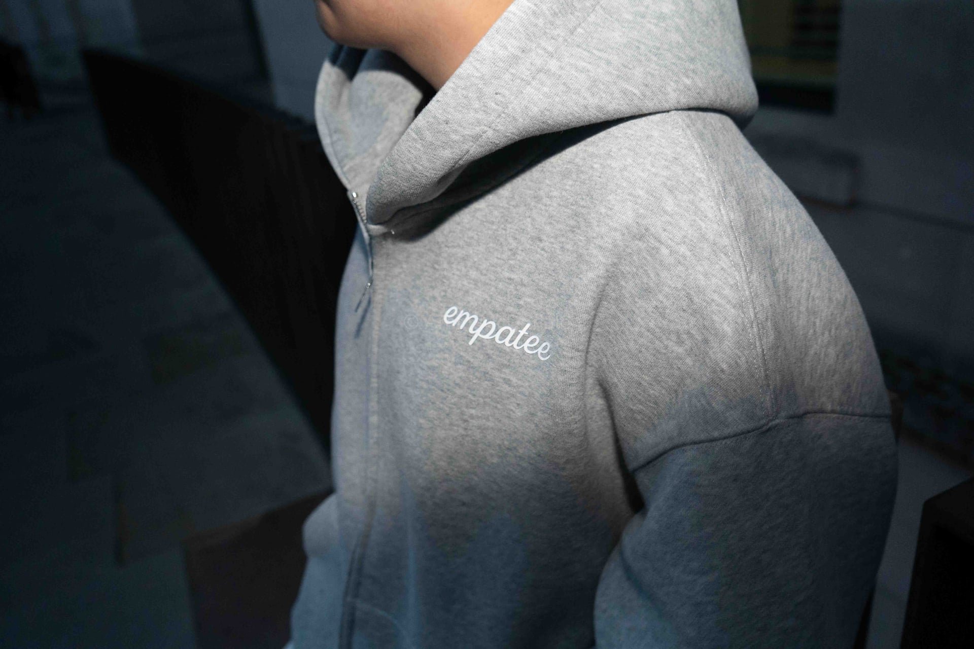 Close-up of a person wearing a gray hoodie with the word 'empatee' embroidered on the chest, viewed from the side and slightly above.