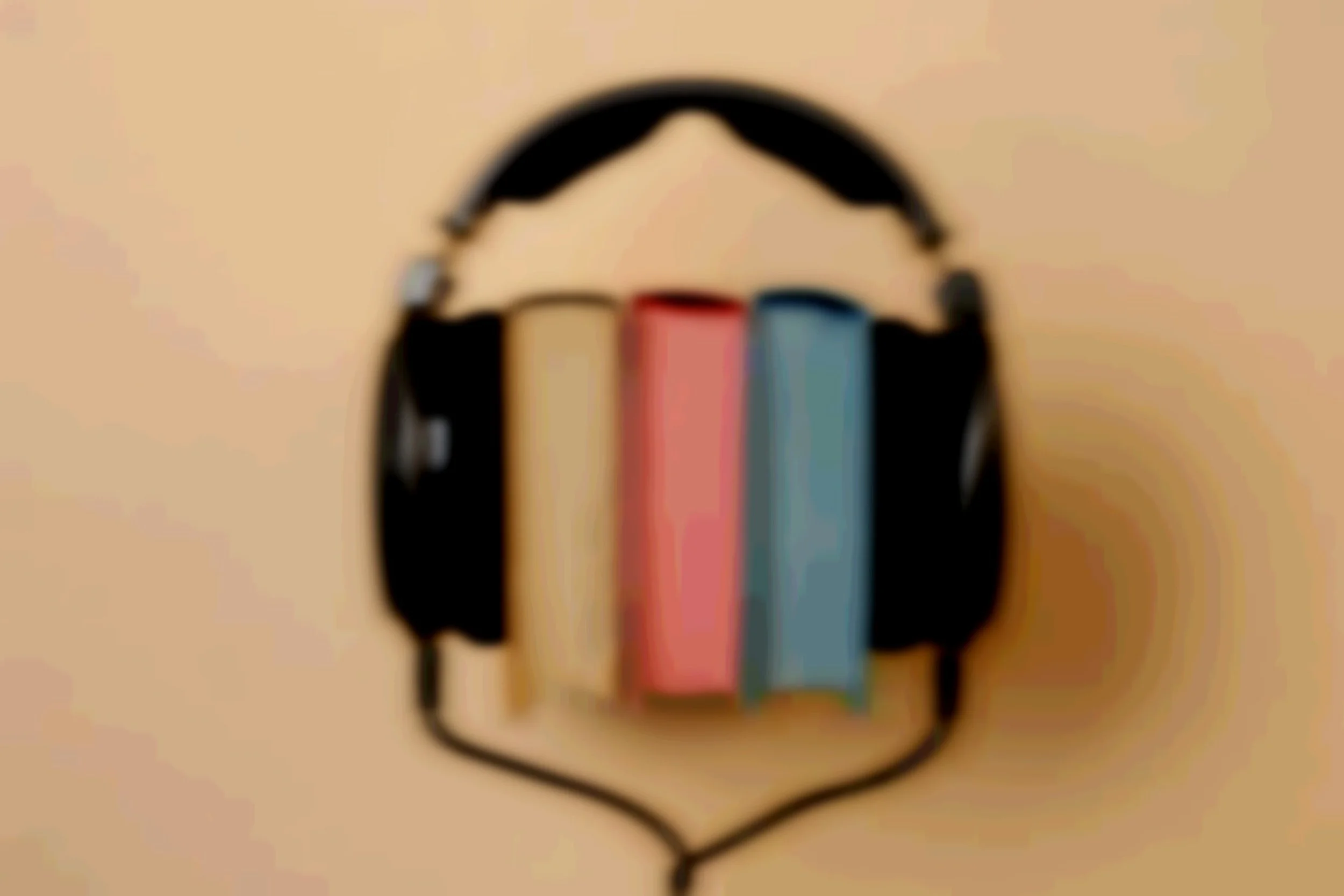 Blurred image of black headphones with three books inside their ear cups on a beige surface.