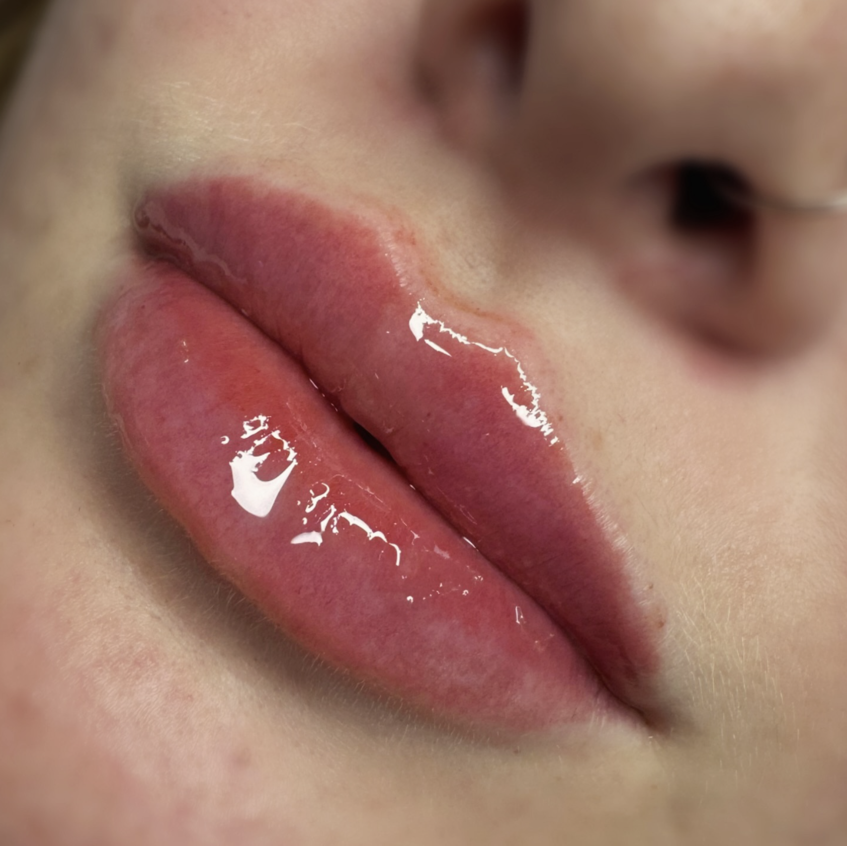 Close-up of a person's glossy, pink lips, slightly parted, with a small amount of water or lip gloss on them.
