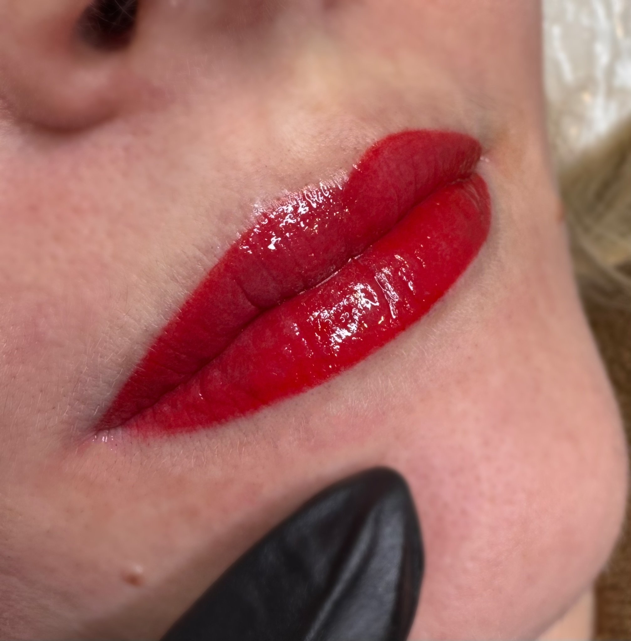 Close-up of a person's lips with glossy red lipstick.