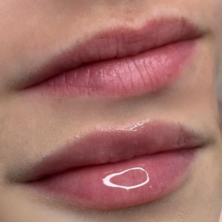 Close-up of two lips, with the bottom lip slightly parted and a small amount of shiny liquid on its surface