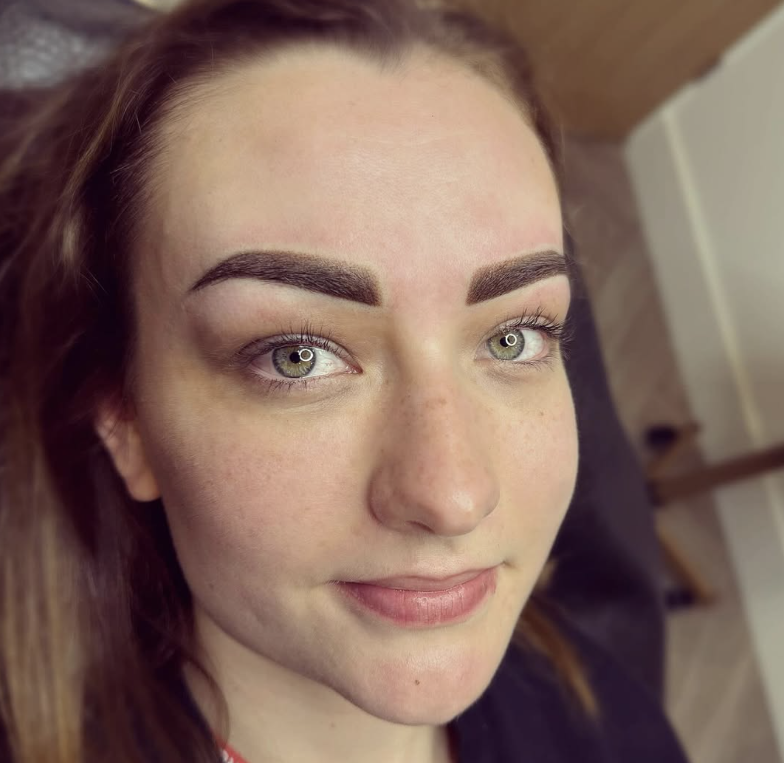 Close-up of a woman with bright green eyes, dark eyebrows, and freckles, smiling softly.