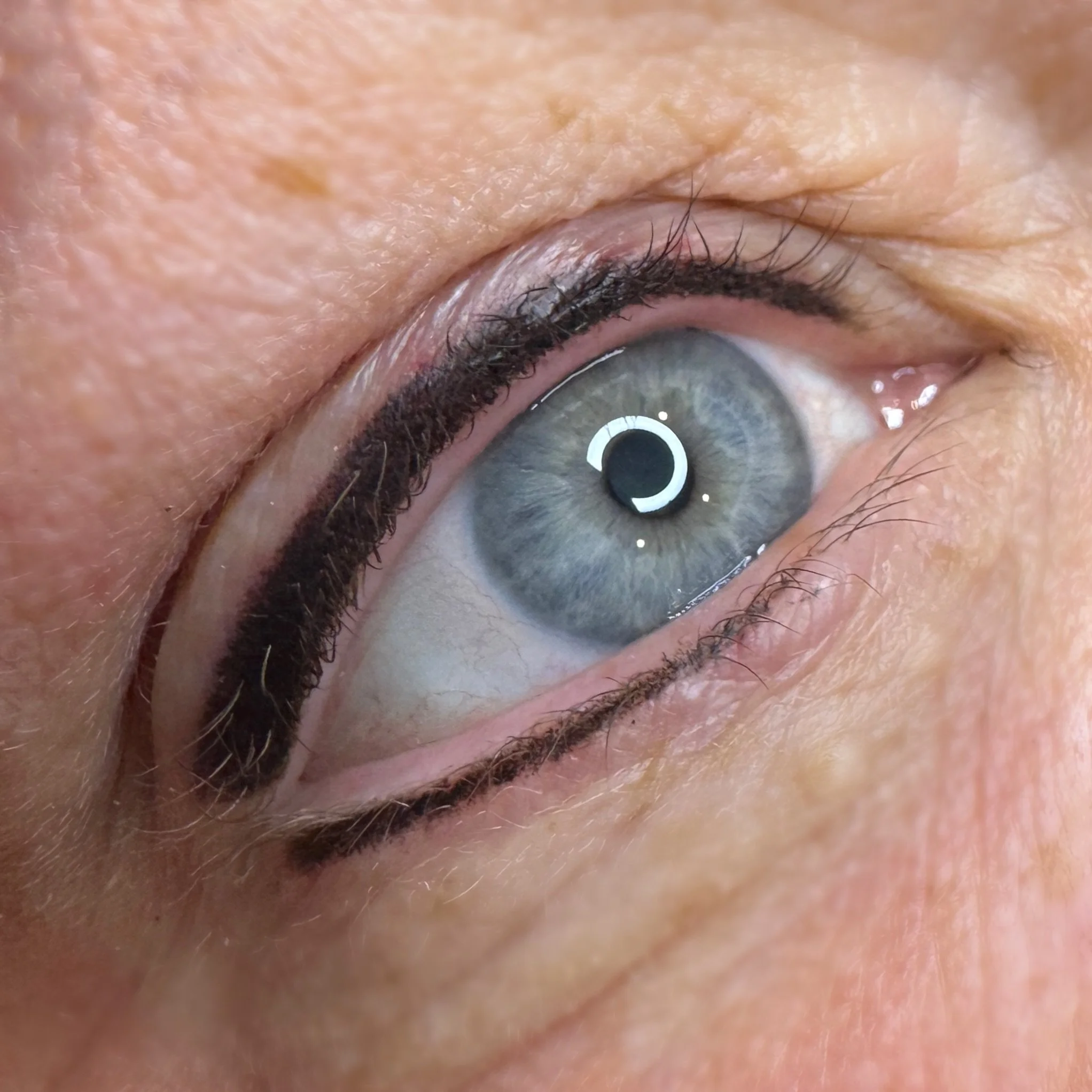 Close-up of a human eye with blue iris, black eyeliner, and light skin around it.