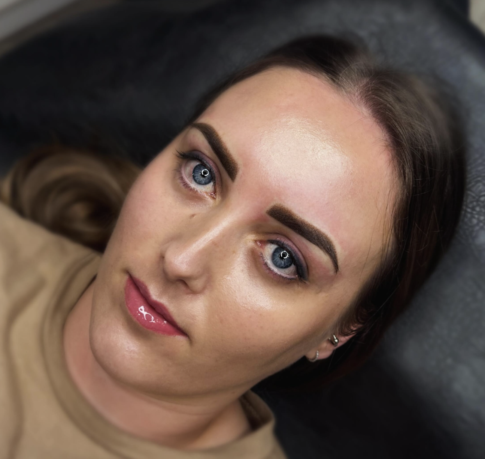 Close-up of a woman's face with makeup, dark eyebrows, blue eyes, and pink lips, lying on a dark surface.