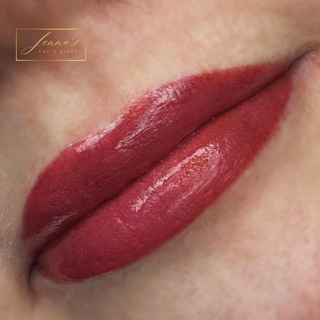 Close-up of lips with glossy red lipstick, smooth skin, and a small logo in the top left corner that reads 'Jenna's PMU & Beauty'.