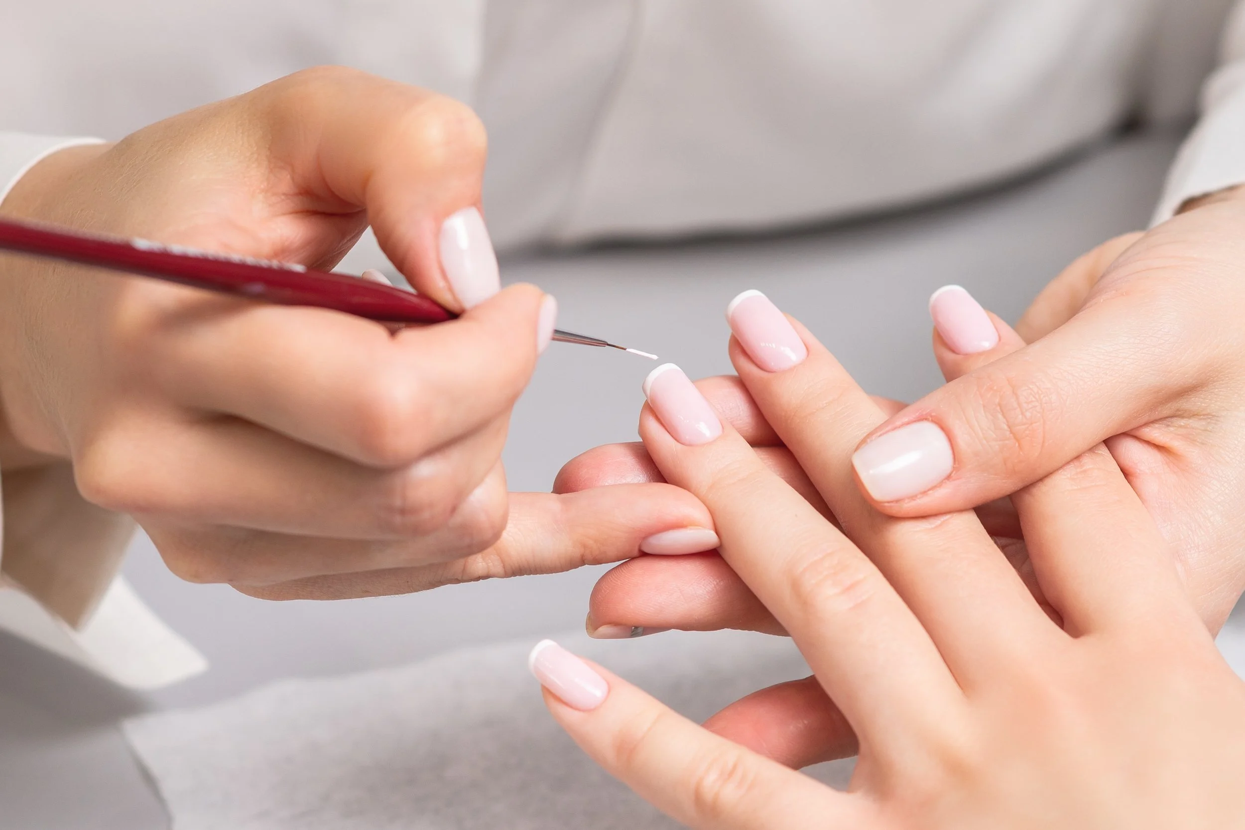 Close-up of a manicurist applying a French manicure to a woman's nails with a small brush.