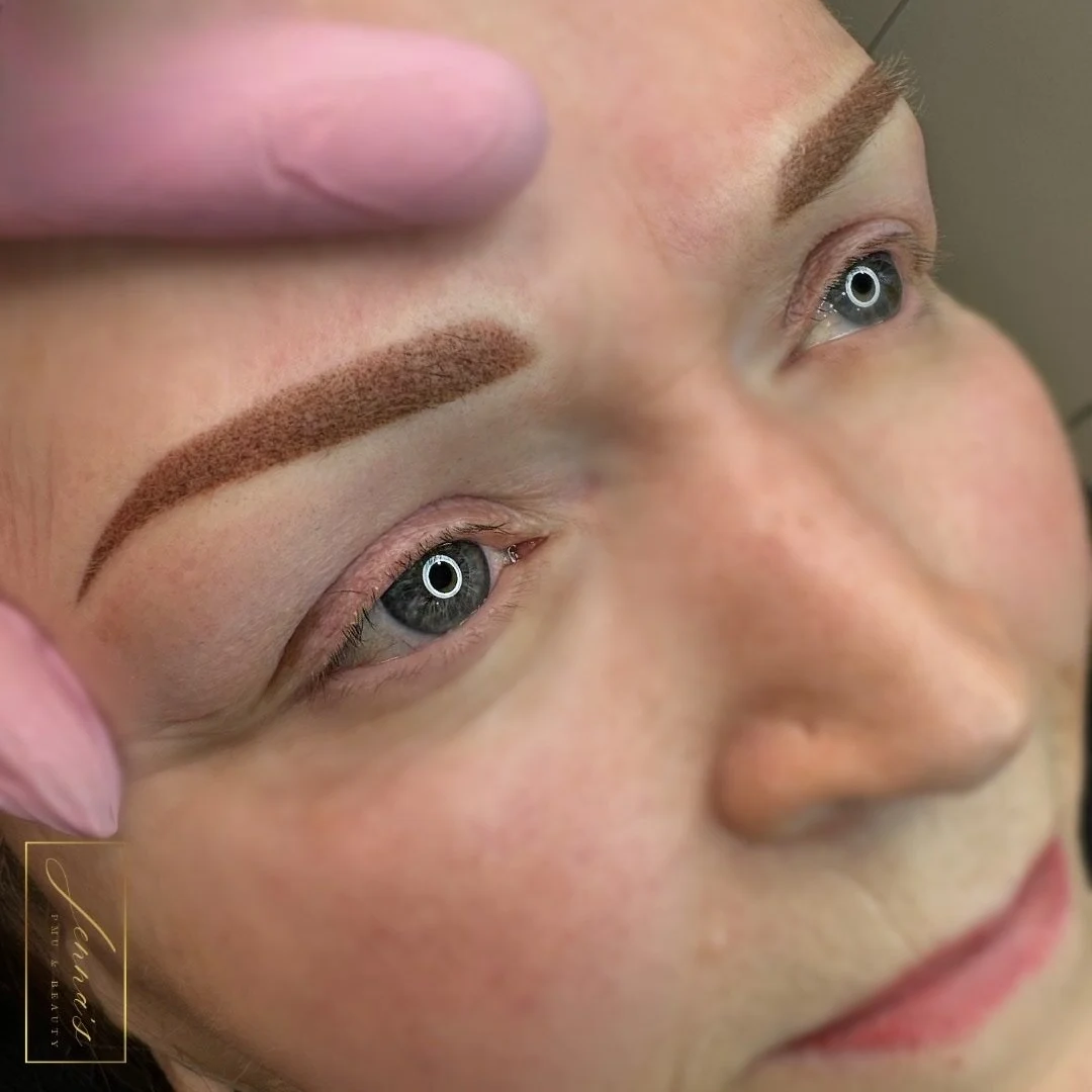 Close-up of a woman with well-defined, filled-in eyebrows, and light makeup, lying down with her eyes open and a slight smile.