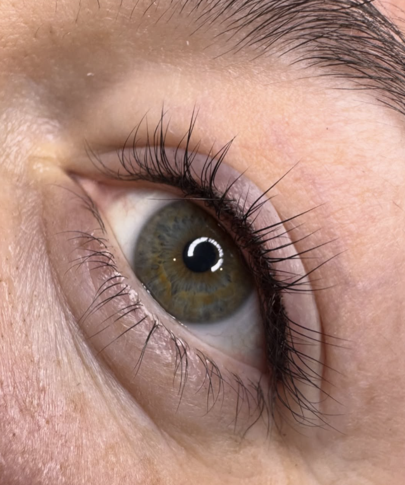 Close-up of a human eye with brown and green iris, long eyelashes, and surrounding skin.