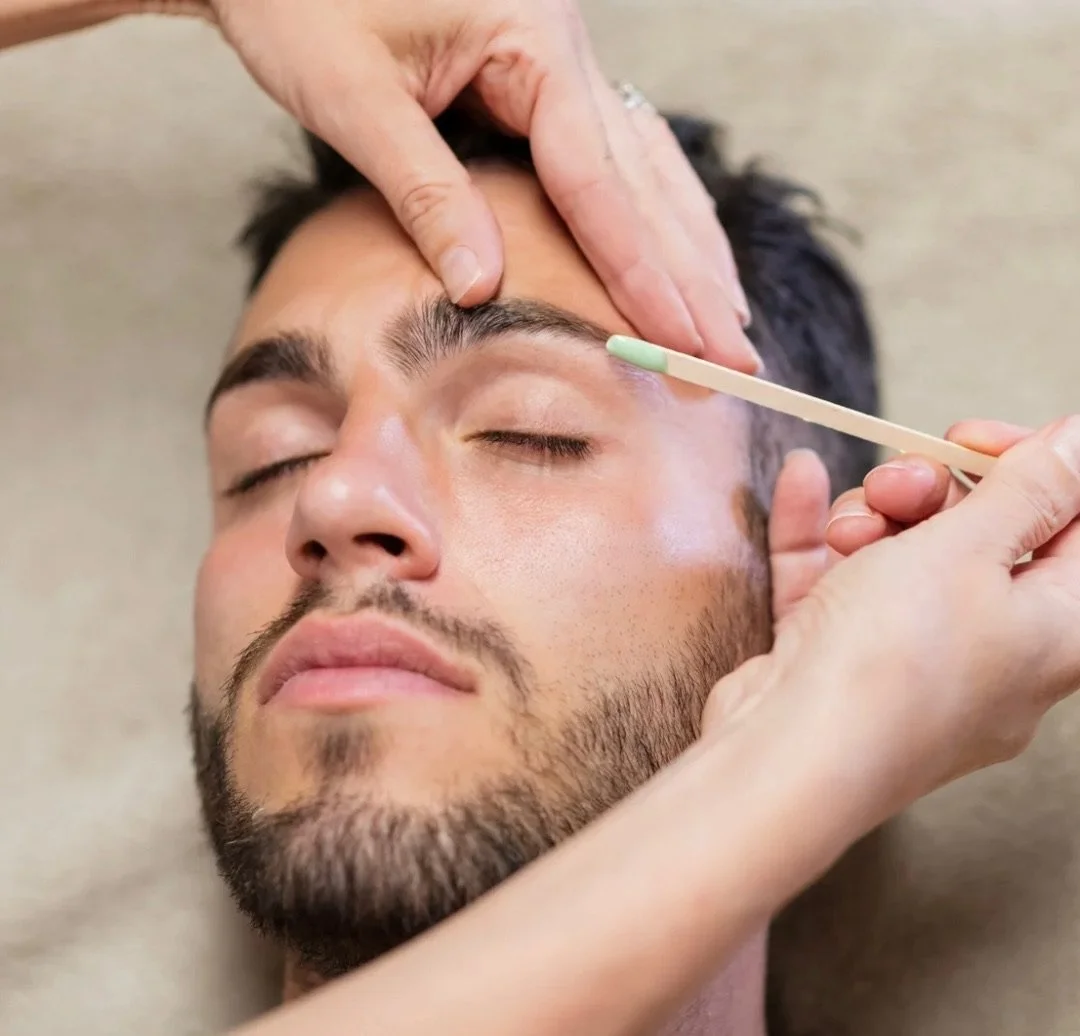 Close-up of a man receiving a facial treatment, with a person's hands applying skincare near his face and a cotton swab in hand.