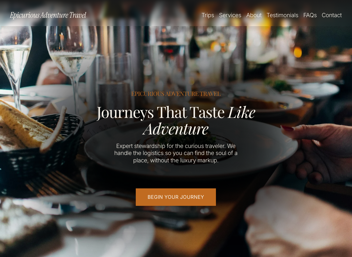The Hero image from the Epicurious Adventure Travel landing page, featuring a close-up of a dining table with plates, glasses of water and wine, bread, and cutlery, set in a restaurant with blurred background.