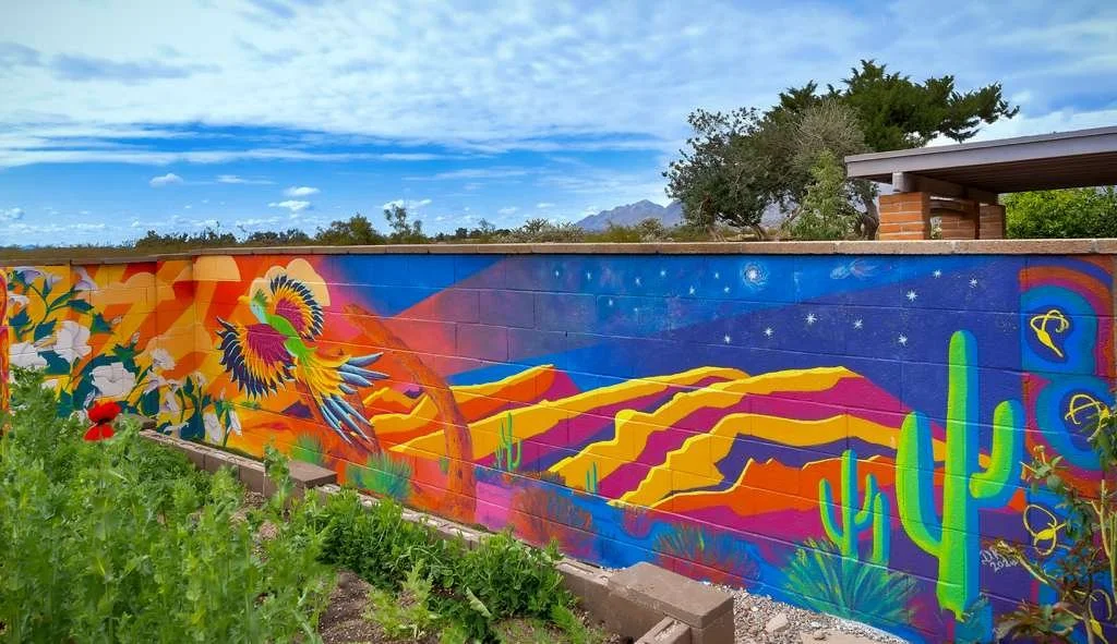 Colorful mural depicting a desert scene with cacti, mountains, and a vibrant bird flying in a sunset sky.