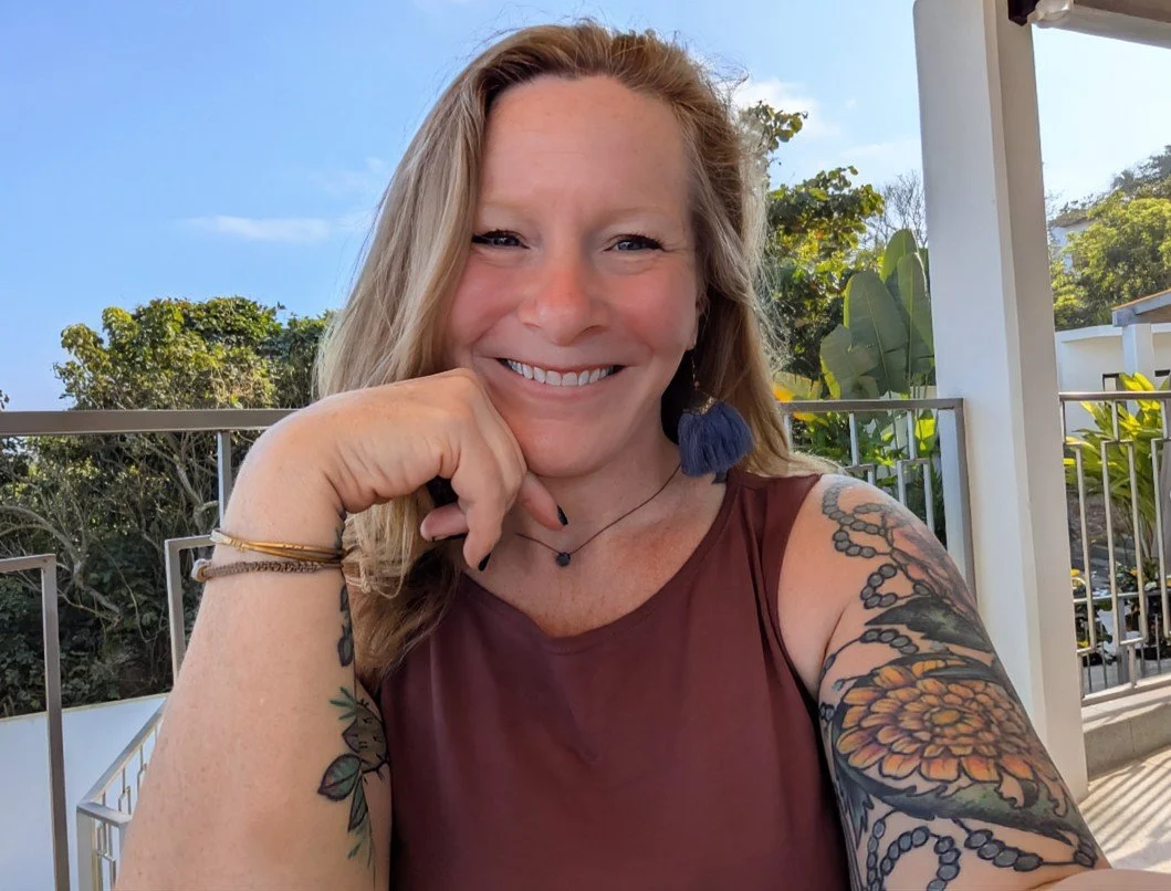 Sand Ruby Studio founder Dawna Kelley, sitting outdoors on a balcony with trees and a blue sky in the background.
