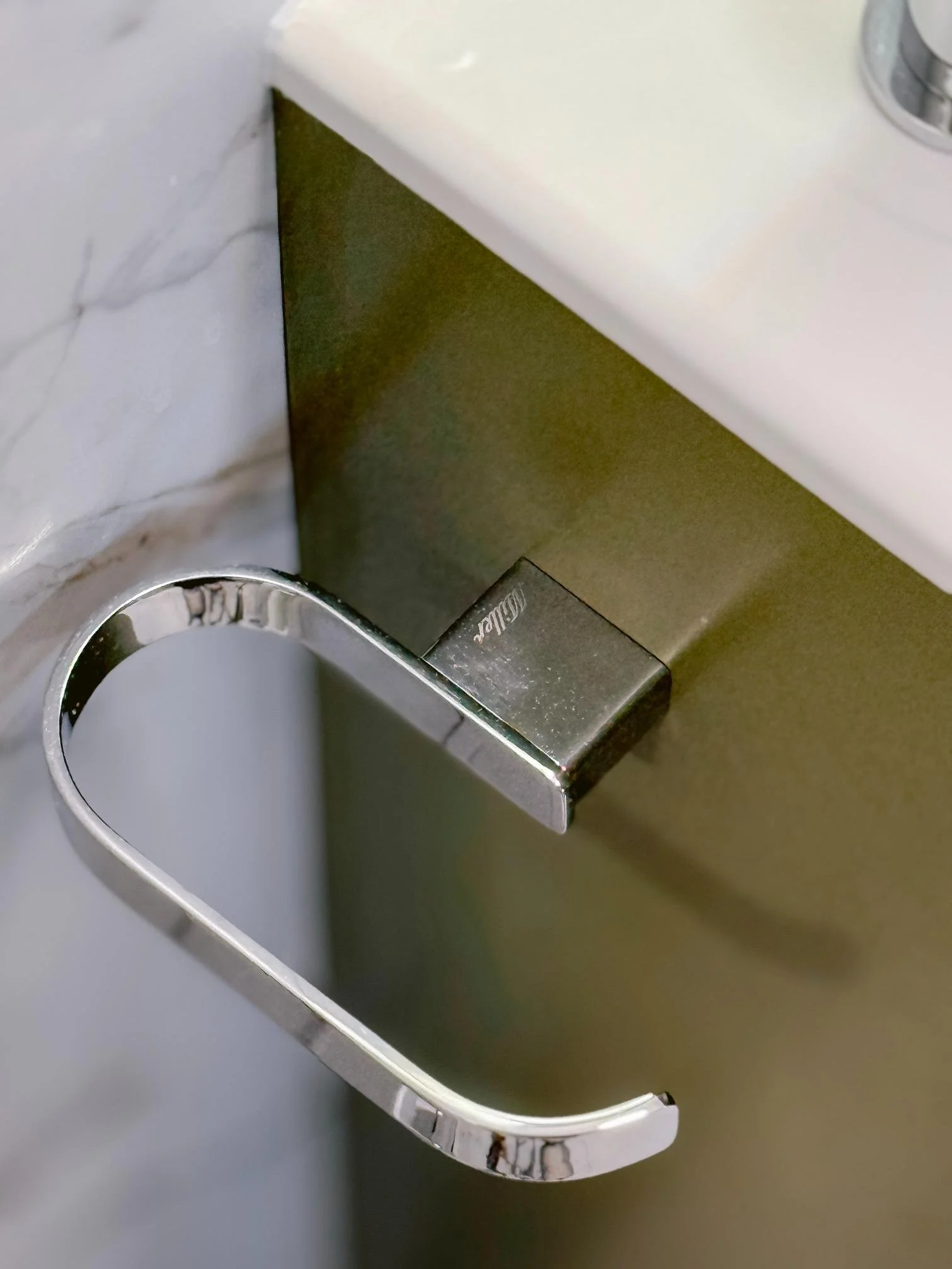 Close-up of a metal handle attached to a drawer or cabinet, with a marble wall and a white surface above.