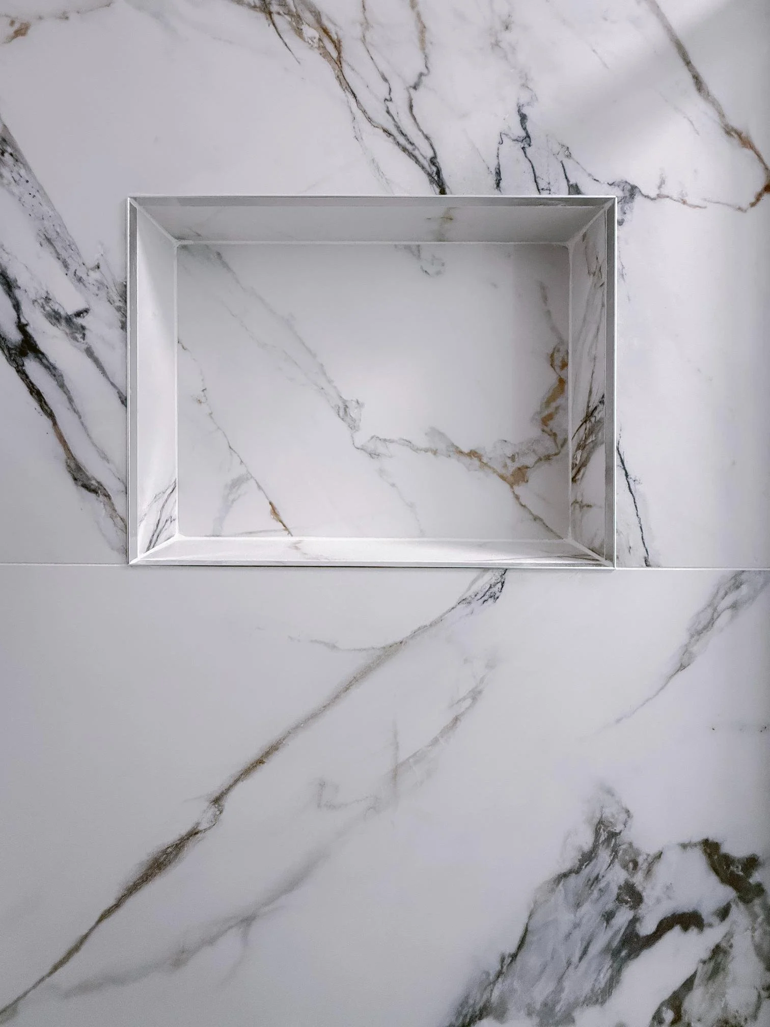 Empty rectangular shower niche set in a marble wall with white and gray veining.