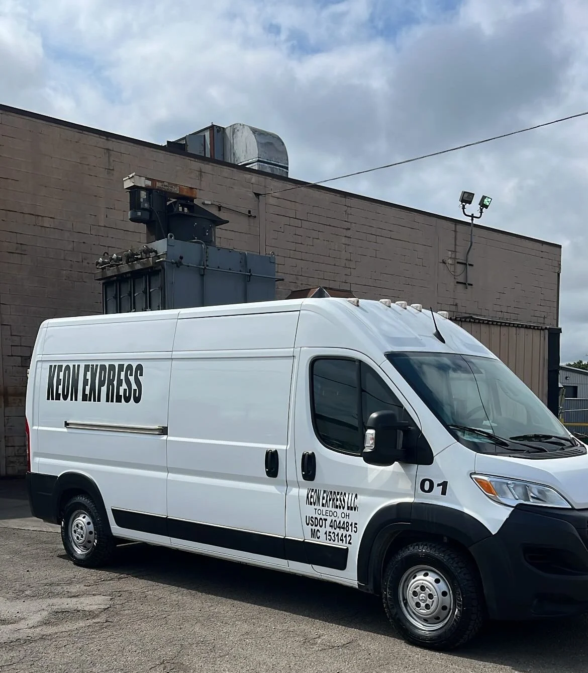 White delivery van with 'Keon Express' branding parked outside an industrial building with HVAC equipment on the roof and a cloudy sky overhead.