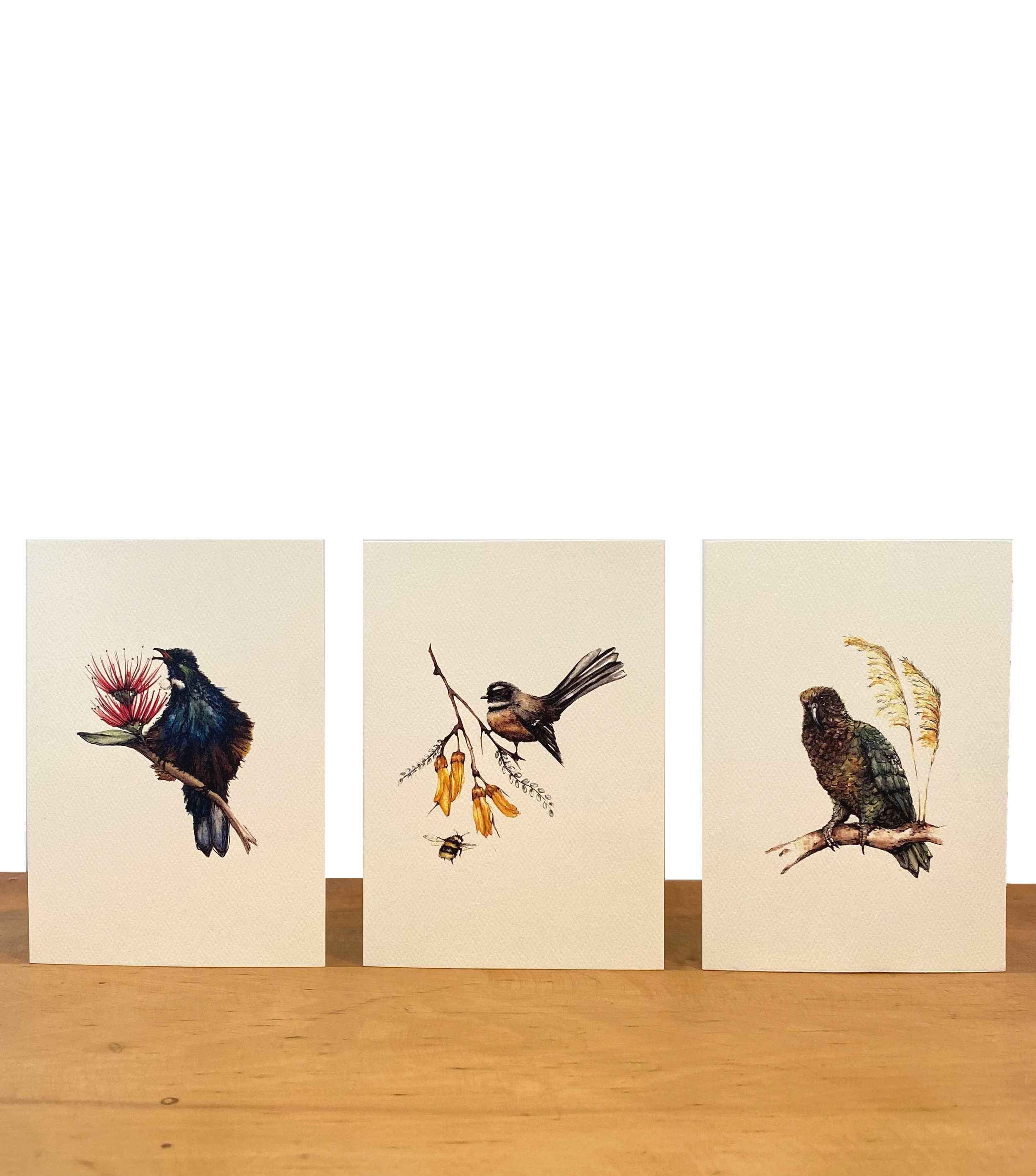 Three cards featuring detailed watercolor paintings of birds and nature scenes, positioned on a wooden surface.