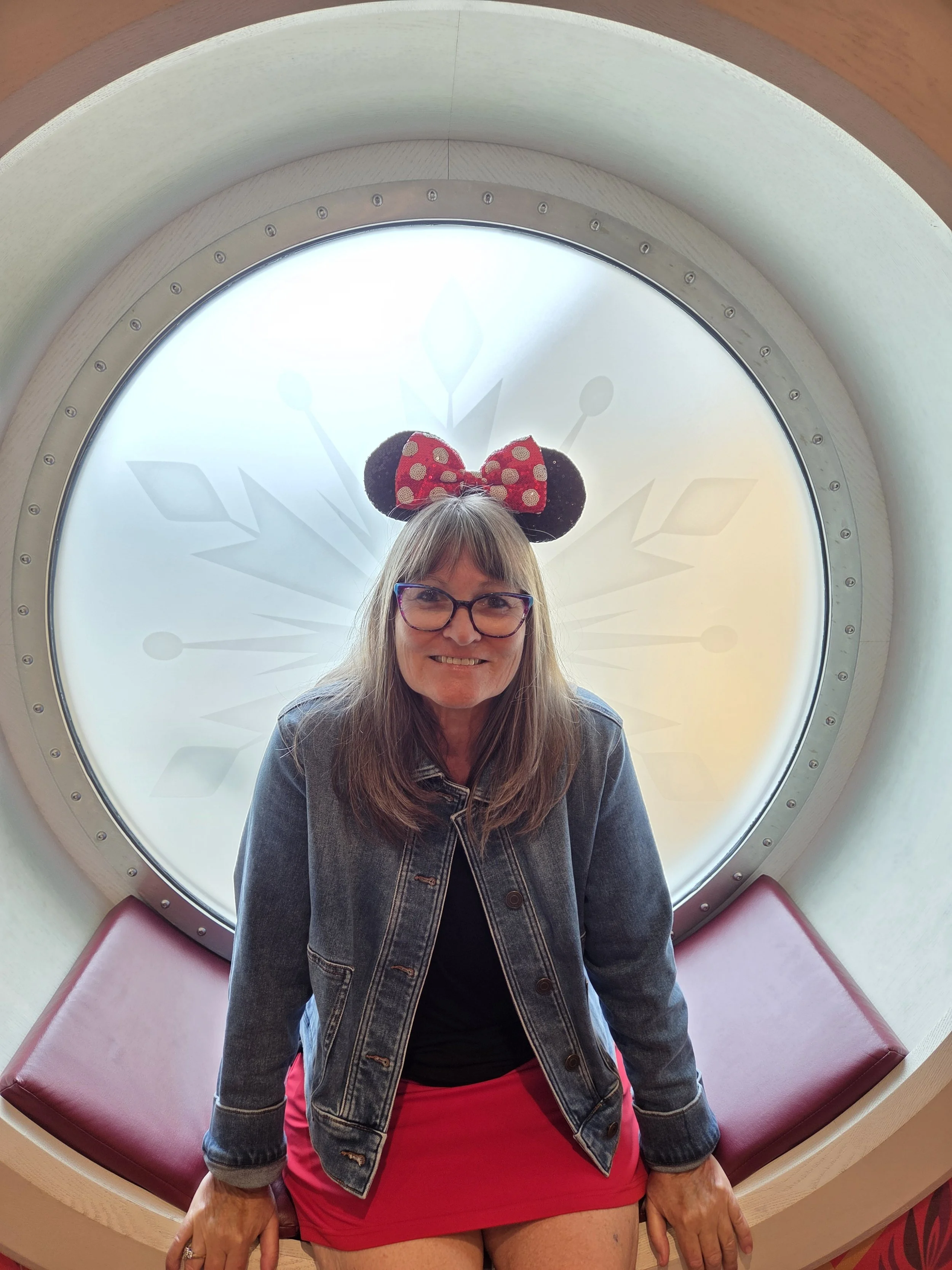Laura Varnau, travel advisor specializing in Disney, sitting by porthole on Disney Wish cruise ship
