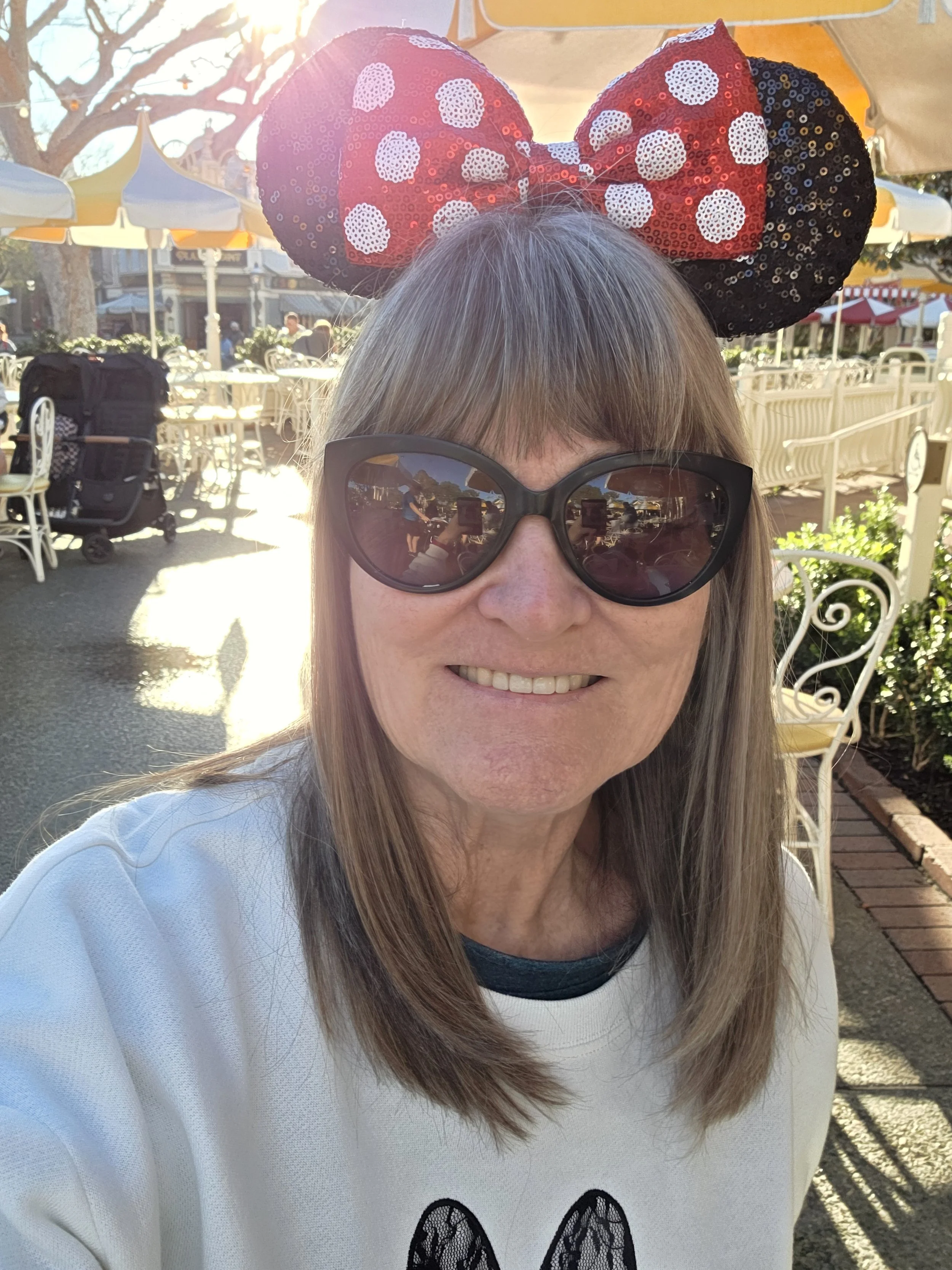 Laura Varnau, travel agent with Wishes and Waves Travel, wearing Mickey ears and sunglasses at an outdoor cafe at Disneyland
