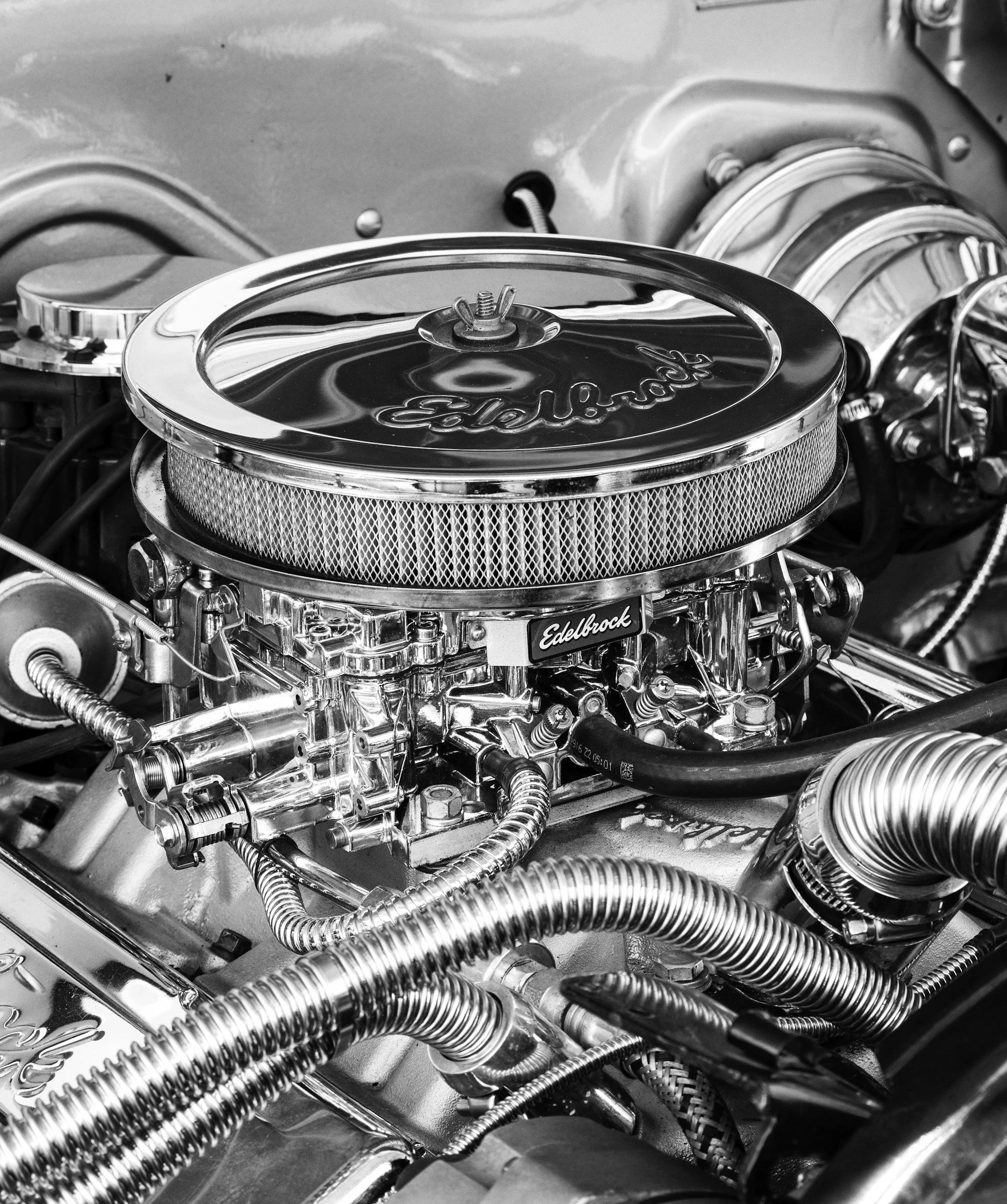 Close-up of a polished Edelbrock carburetor on a car engine with chrome-plated components and wiring.