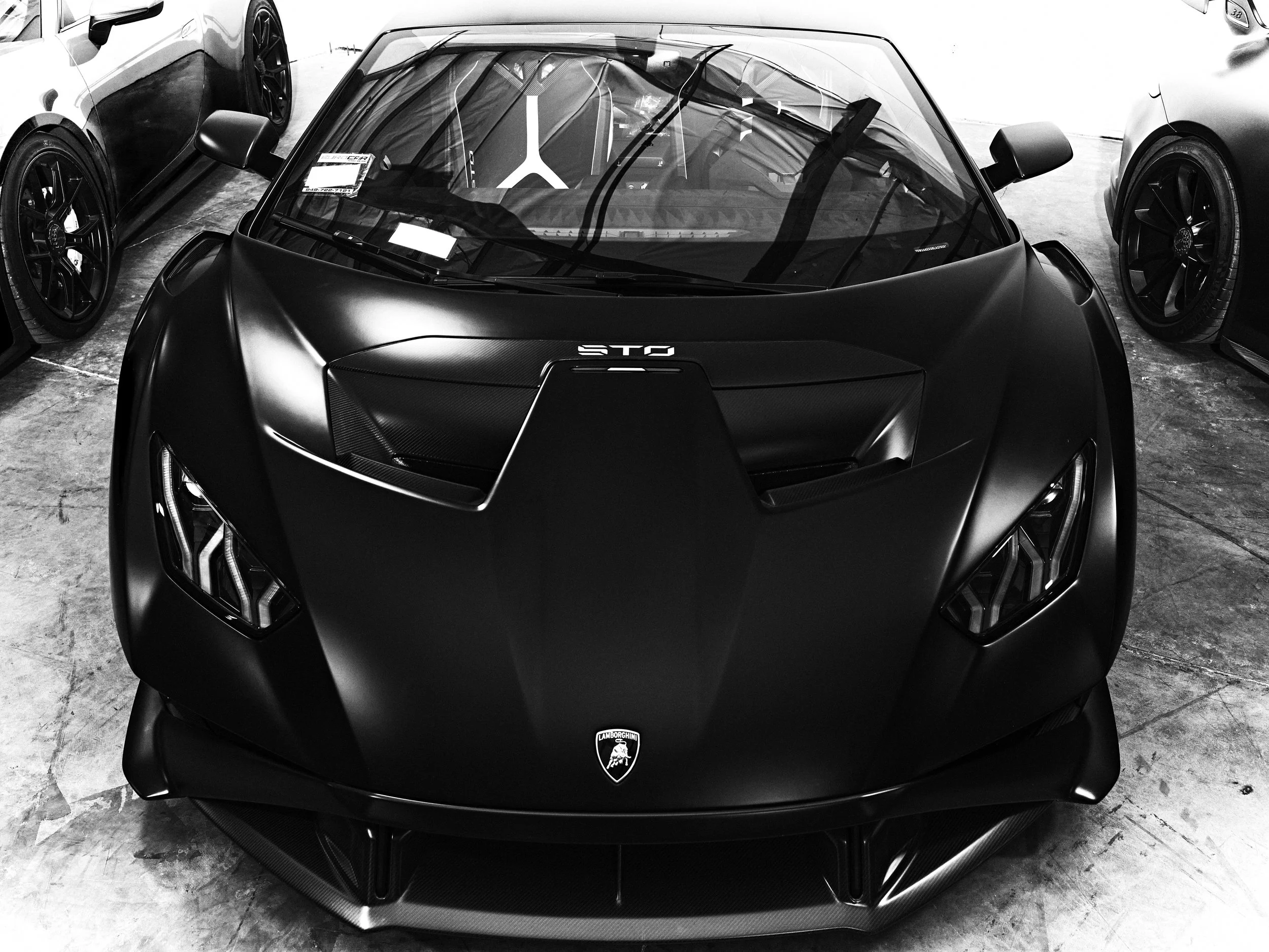 Black sports car with Lamborghini logo and 'S' badge on the front, parked indoors among other vehicles.