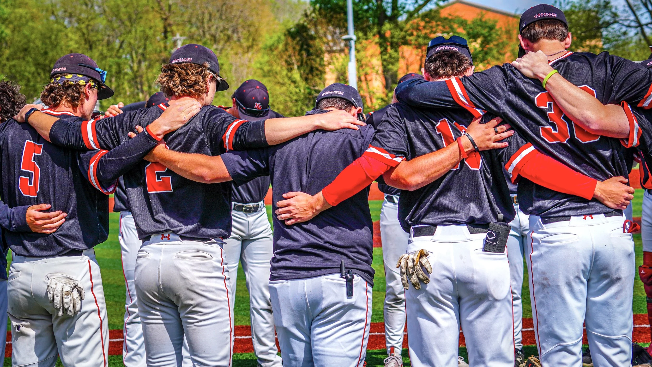 A group of baseball players in black and red uniforms huddling together with arms around each other on a baseball field.