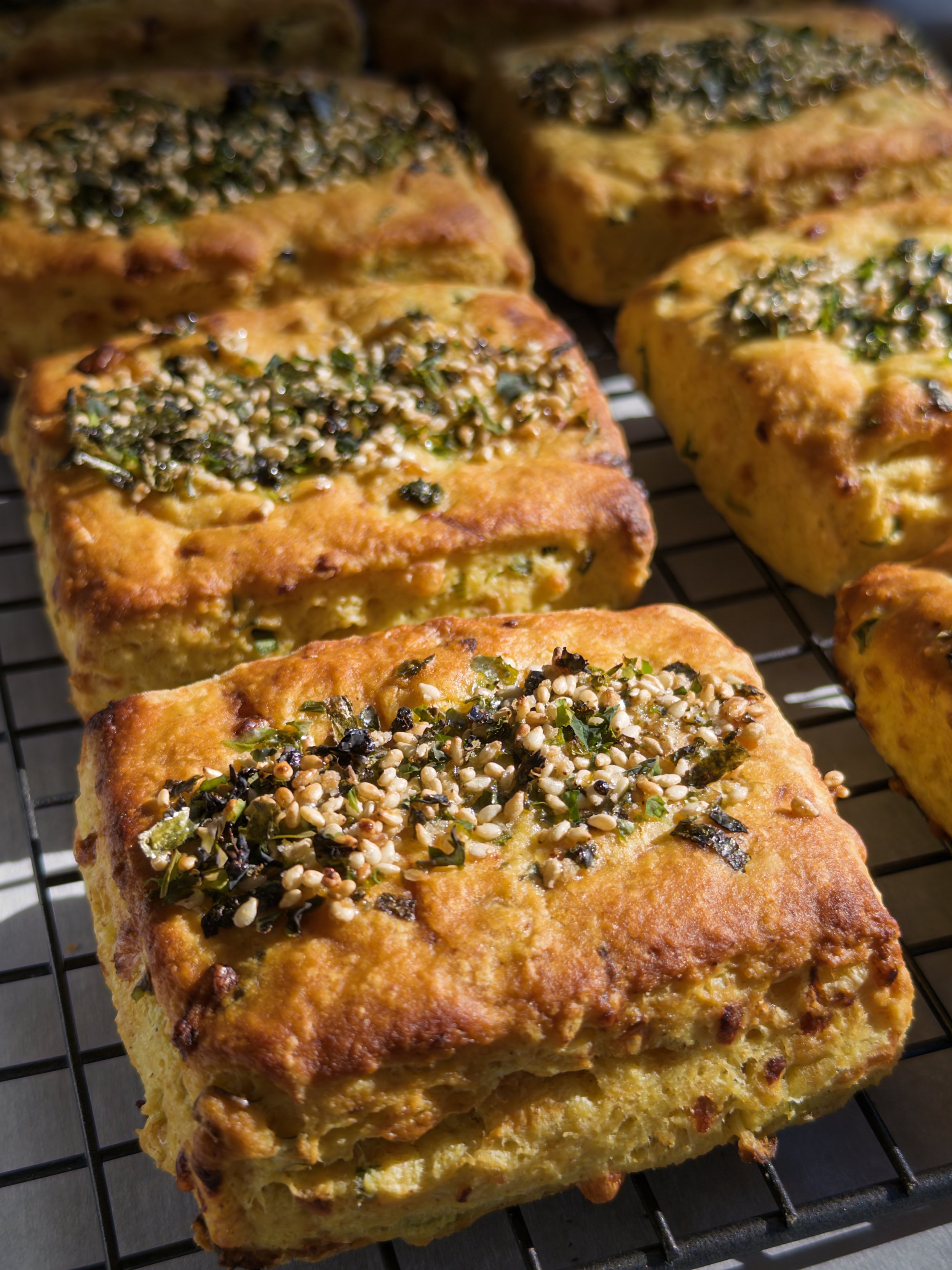 Close-up of baked garlic bread topped with herbs, chopped garlic, and melted cheese on a wire rack.