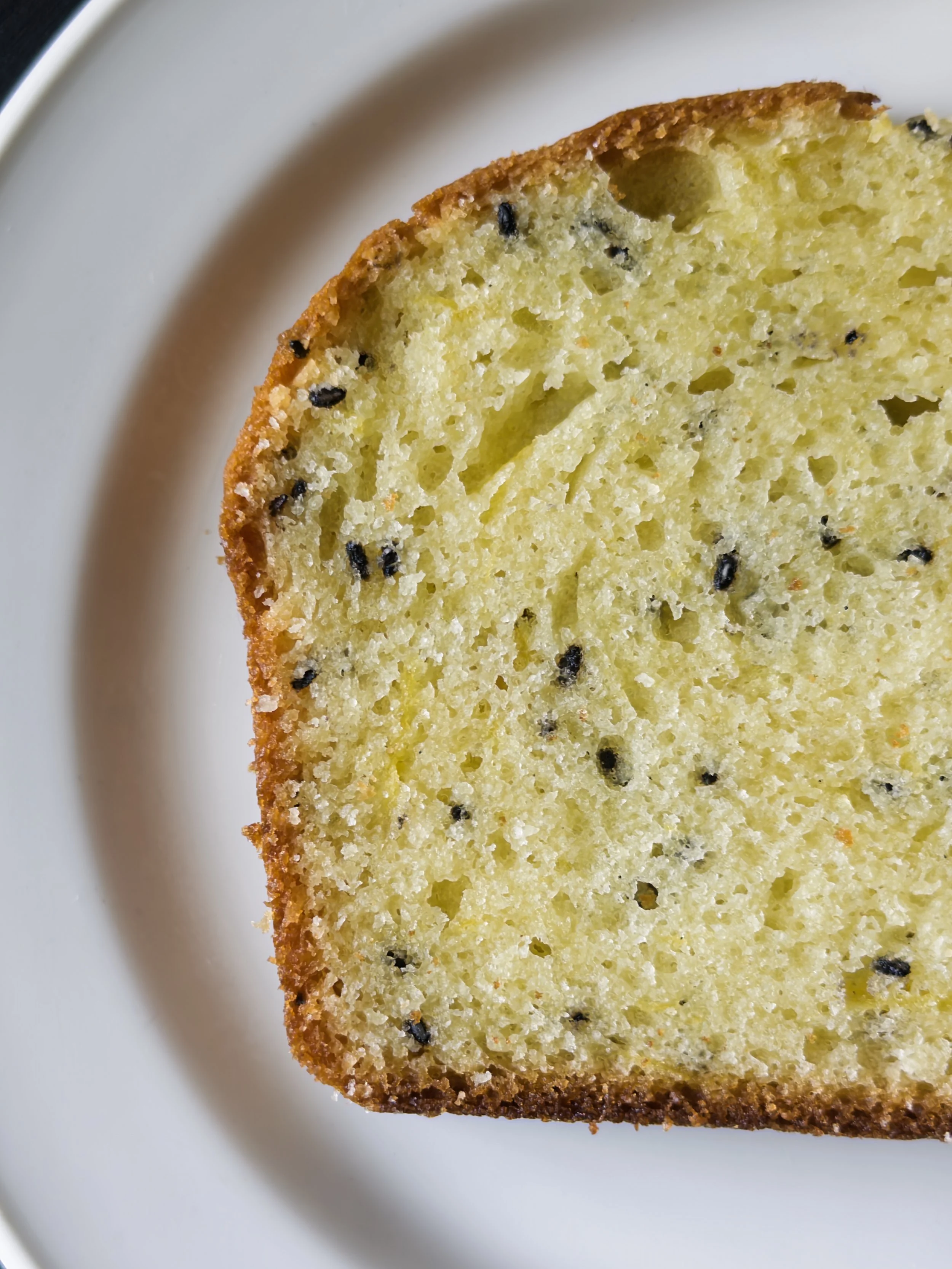 Close-up of a slice of yellow cake with black sesame seeds on a white plate.