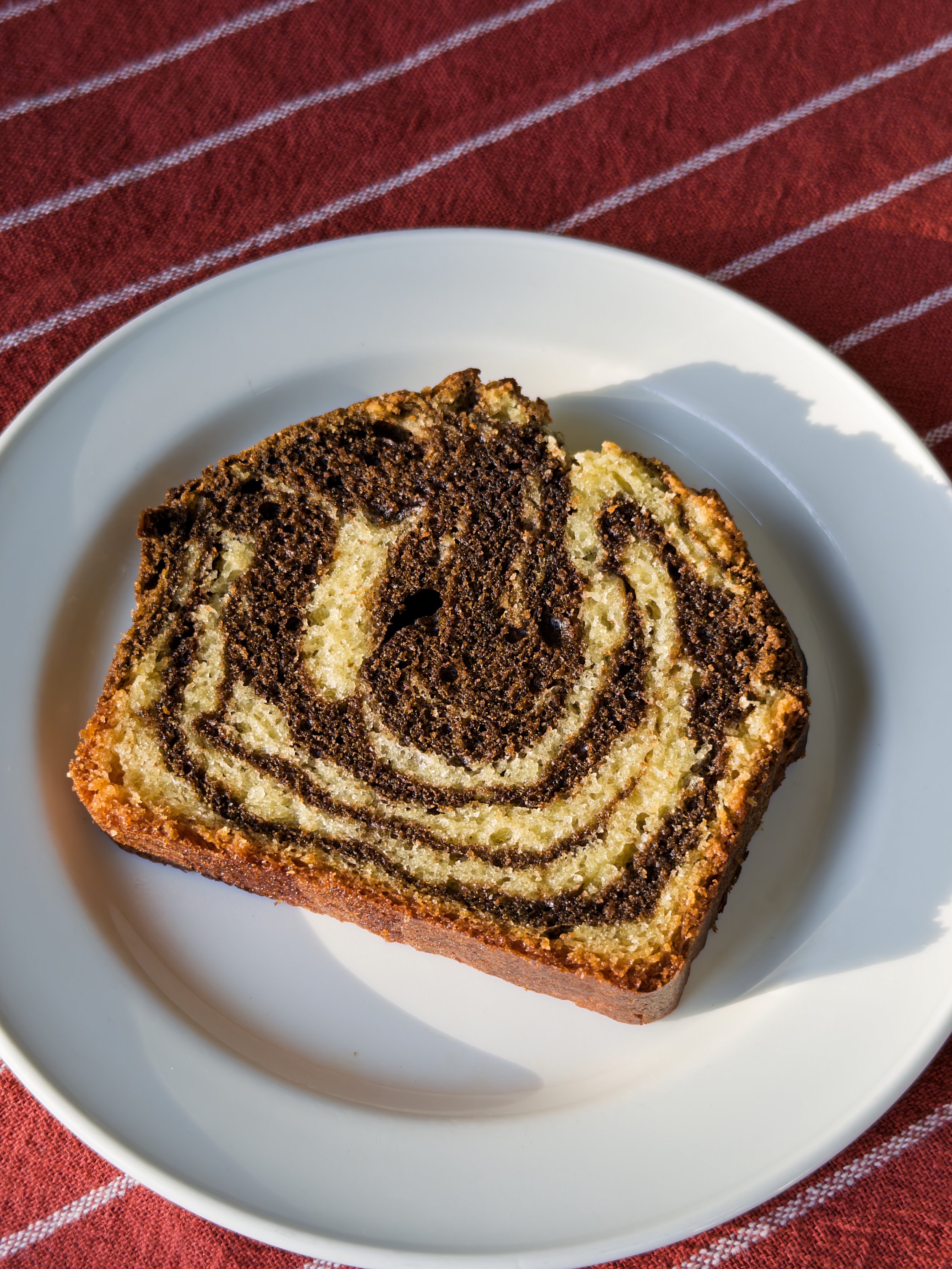 Slice of marble cake with vanilla and chocolate swirls on a white plate with a red striped cloth underneath.