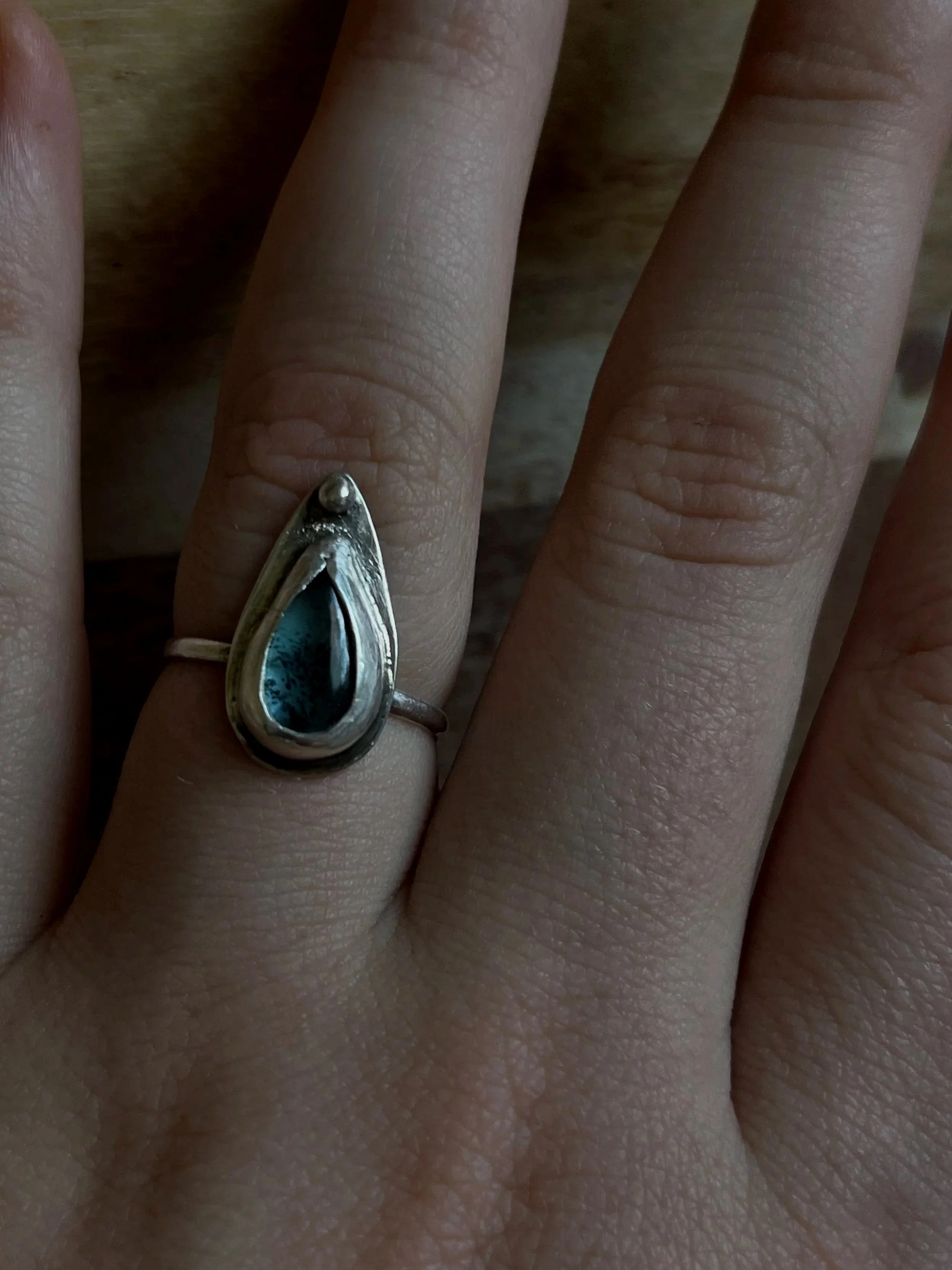 Close-up of a person's hand wearing a silver ring with a teardrop-shaped blue and black gemstone.