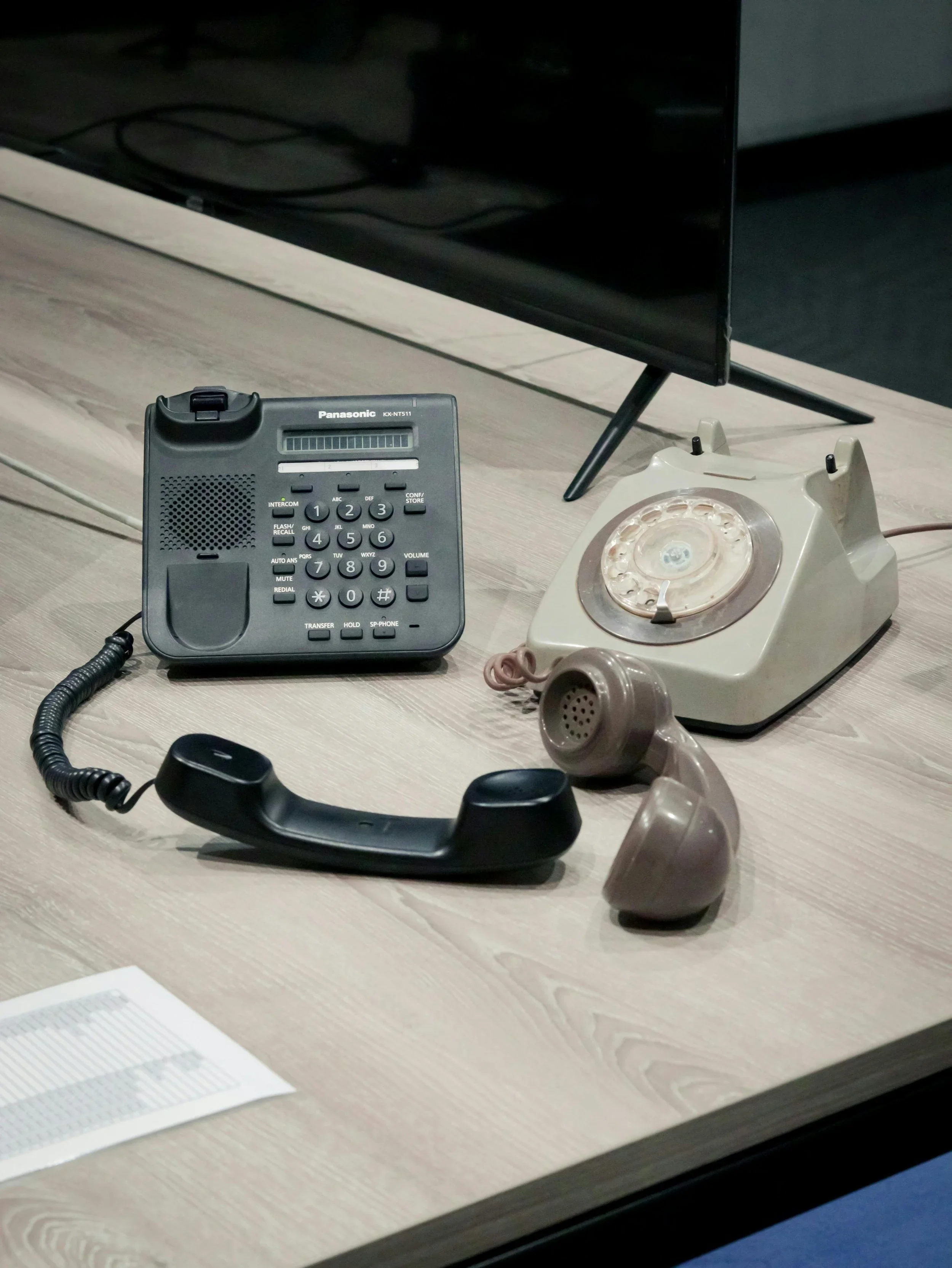 Old rotary dial telephone and a modern digital office phone on a desk near a vintage rotary phone.