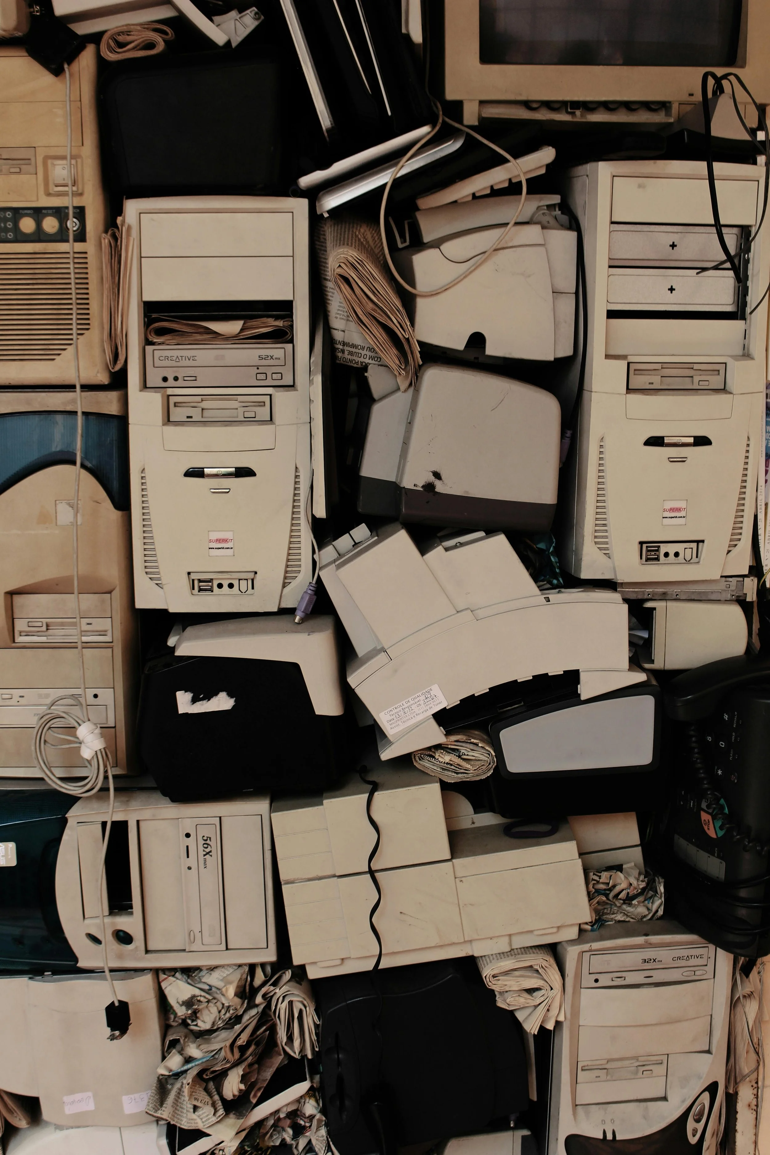 A pile of vintage computer towers, printers, and electronic devices, with some paper and tangled cords.