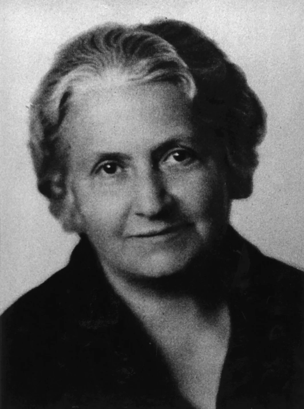 Black and white portrait of an older woman with short, wavy hair, wearing a dark top.