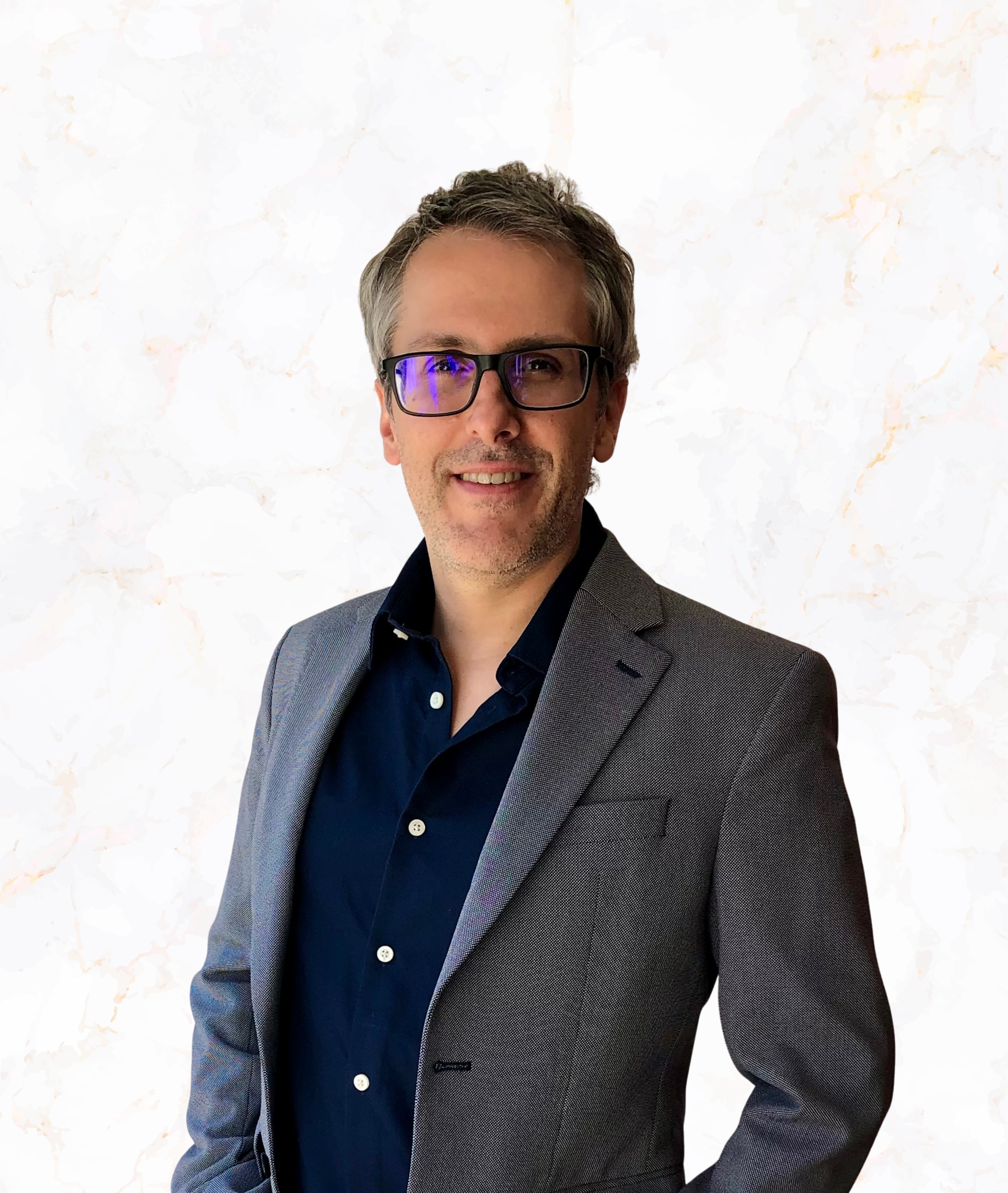 A man with glasses and gray hair in a business suit, smiling, against a plain light background.