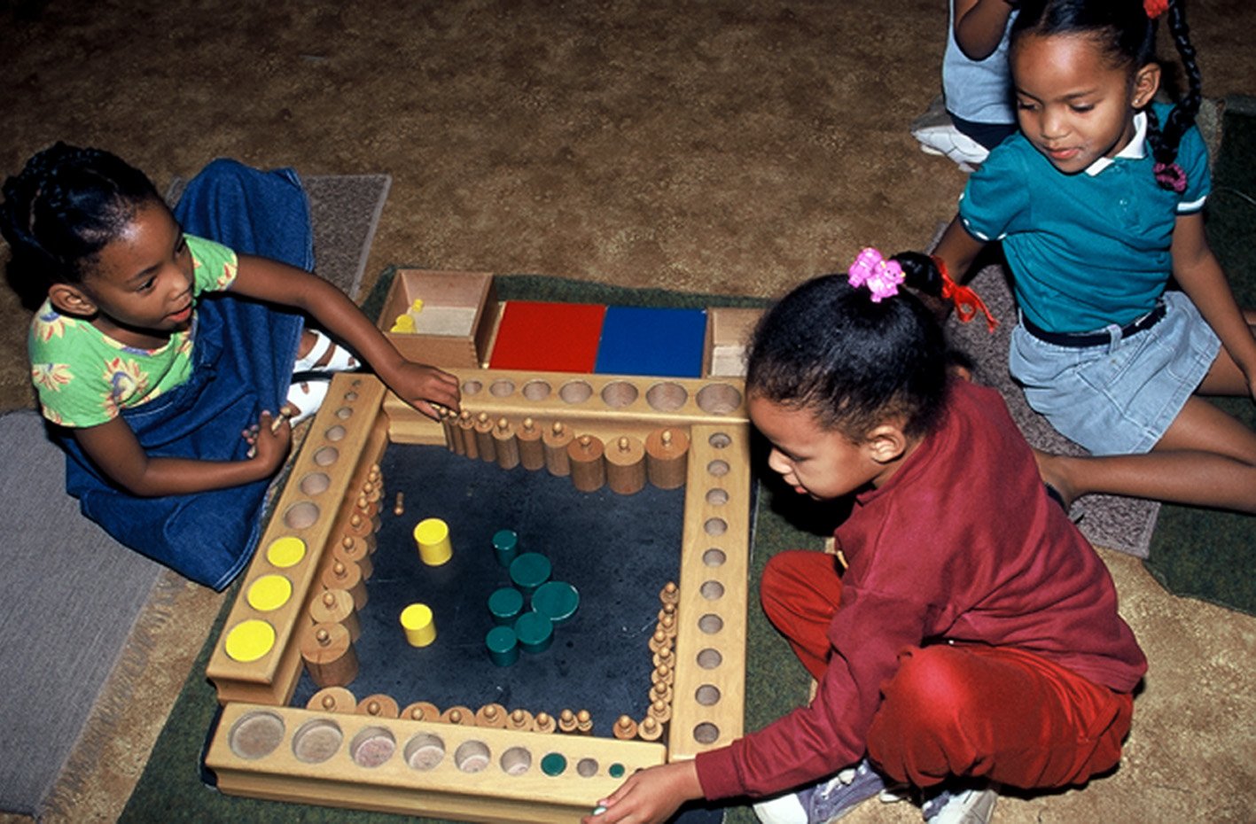 Children playing carrom on the floor indoors.