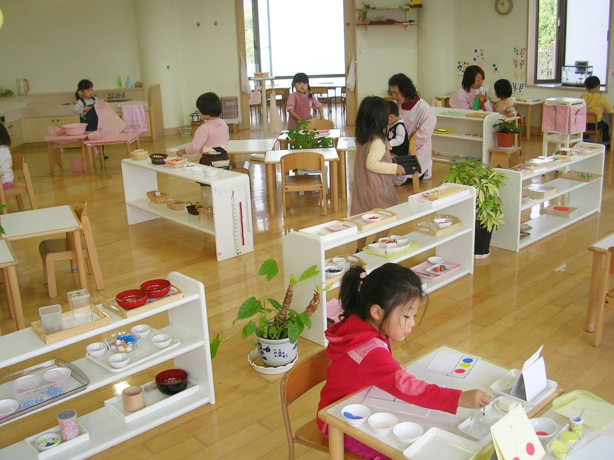 Children participating in a role-playing activity at a classroom pretending to be in a store or restaurant, with shelves displaying various toy or pretend food items and decorations.