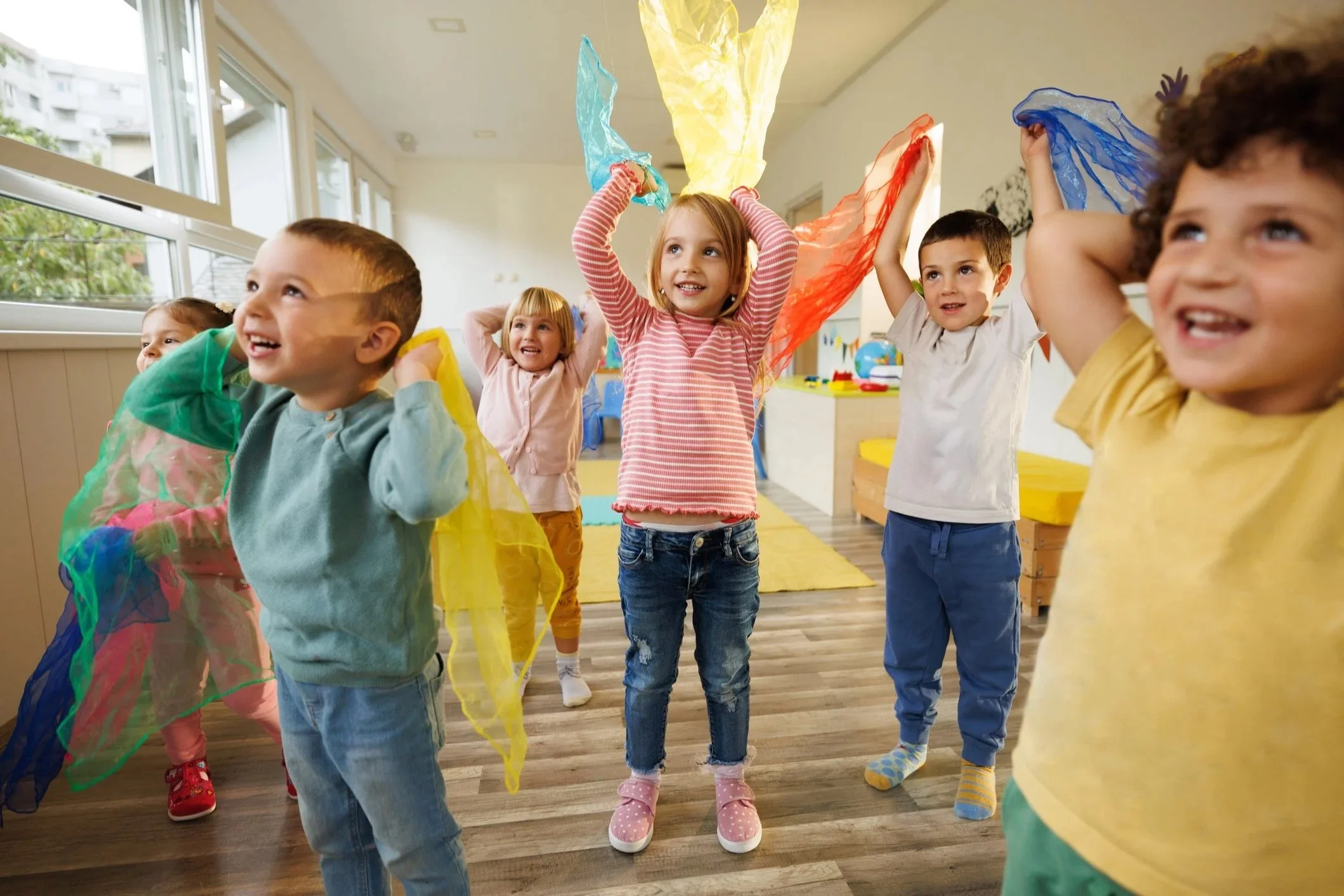 Children playing with colorful scarves in a bright indoor playroom.
