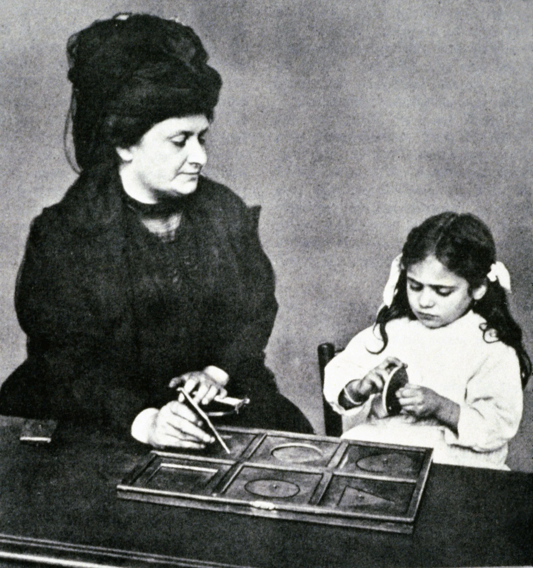 A woman and a young girl playing checkers. The woman is wearing a dark dress and a large hat, looking at the game board, while the girl has pigtails with ribbons and is holding a checker piece, focused on the game.