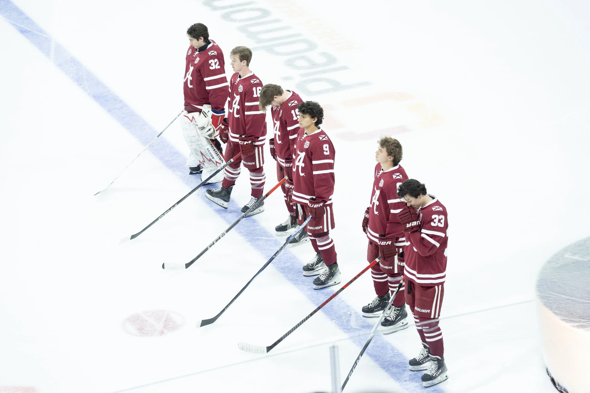 Ice hockey team in red jerseys standing on ice rink with heads bowed.