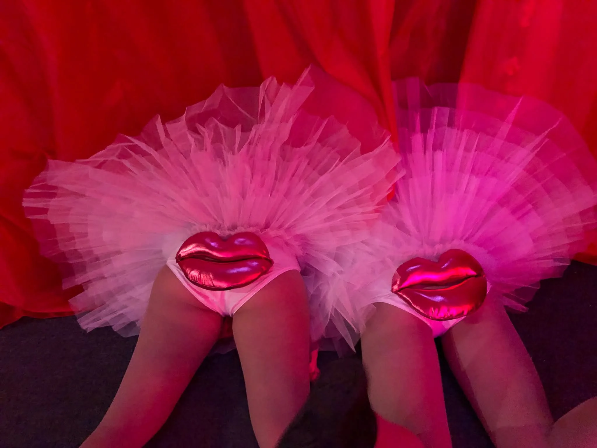 Close-up photo of a person wearing a pink tutu skirt with red and pink heart-shaped metallic balloons.