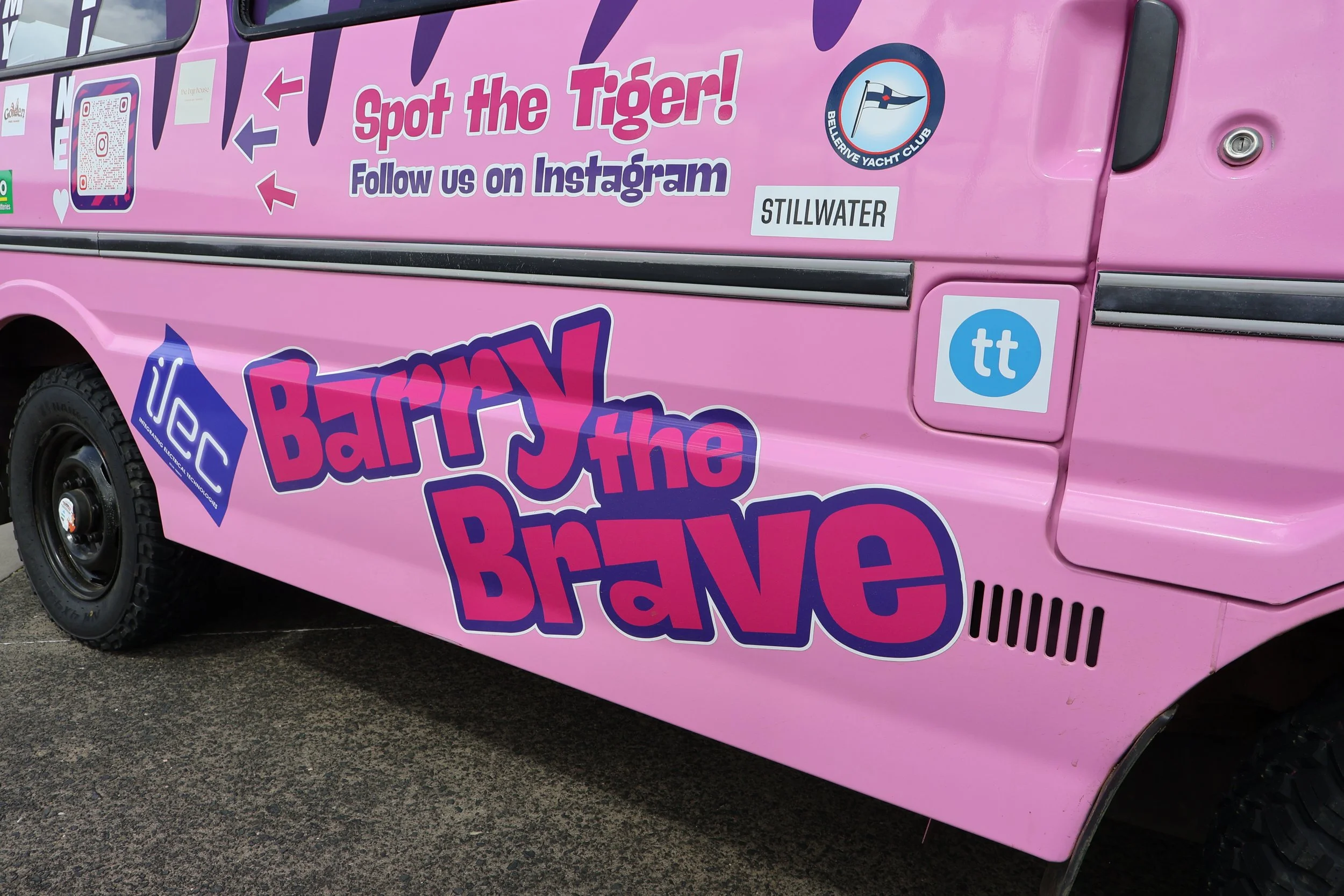 Pink vehicle with summer-themed stickers and promotional text, including a message to follow on Instagram, a logo of Bellerive Yacht Club, and the words 'Spot the Tiger!'