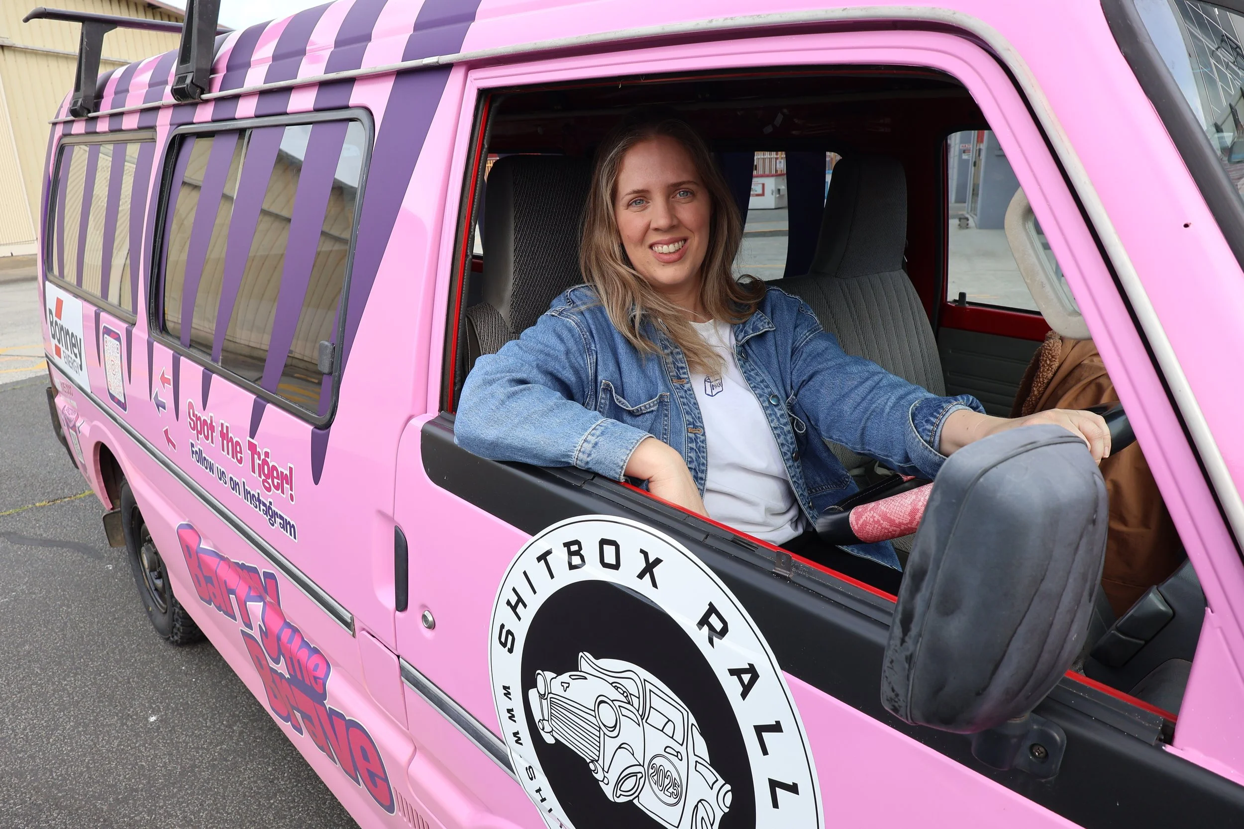 A woman sitting in a pink and purple vehicle with promotional decals, smiling at the camera.