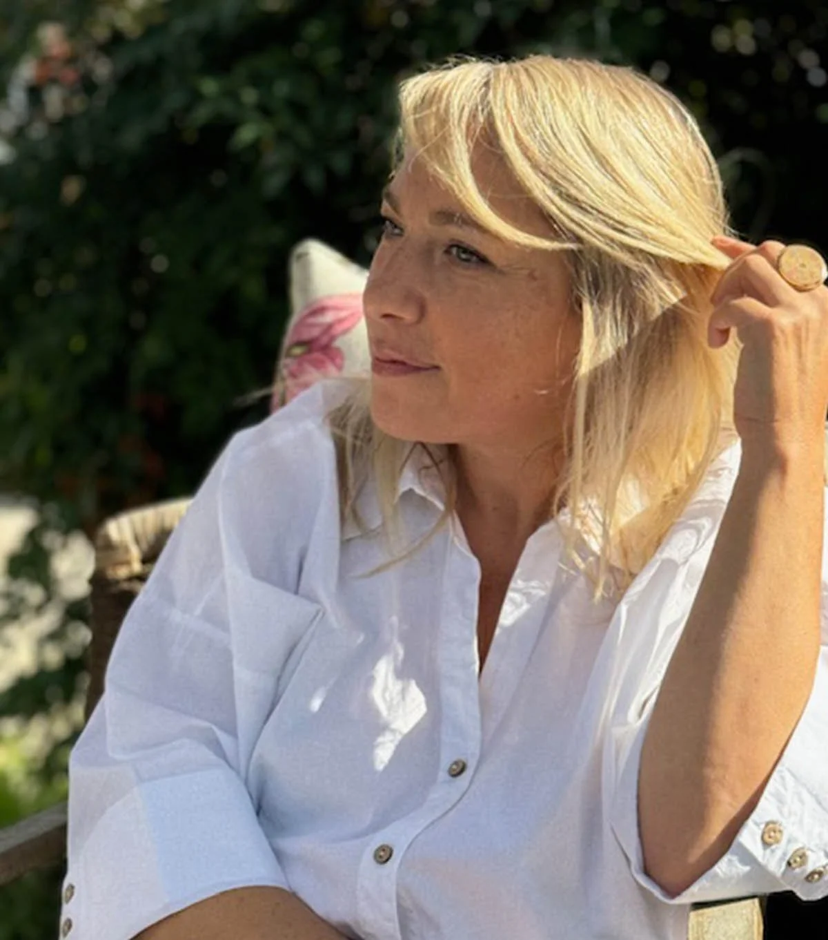 Silvia Maggio. Una donna con capelli biondi e corti, indossa una camicia bianca, si trova all'aperto in un ambiente con vegetazione e sembra godersi il sole.