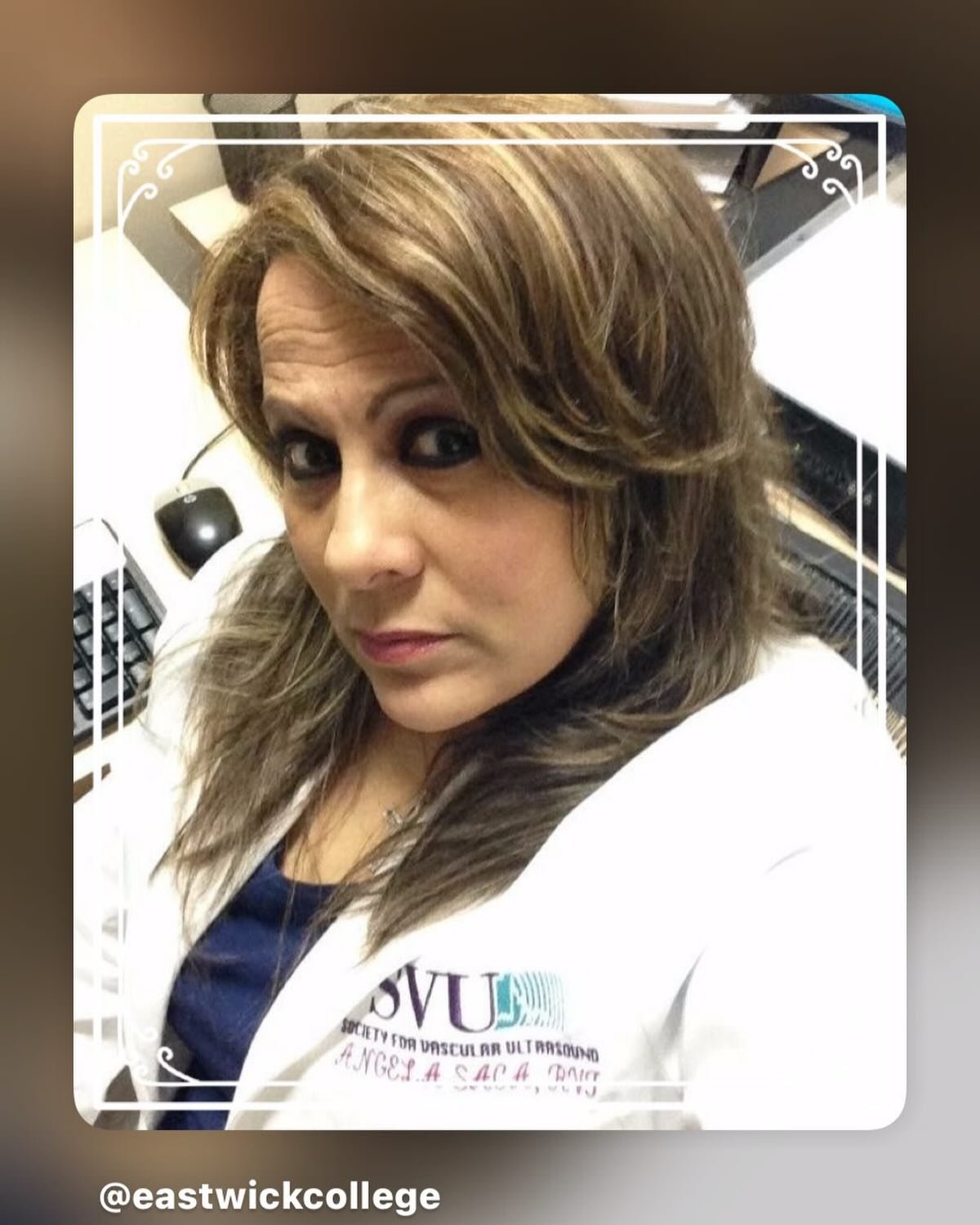 A woman with light brown, styled hair in a medical uniform, sitting in an office or clinic environment.