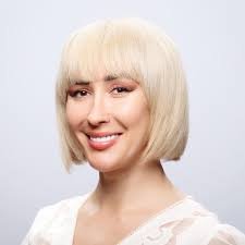 Portrait of a woman with short platinum blonde hair, smiling, wearing a white top.