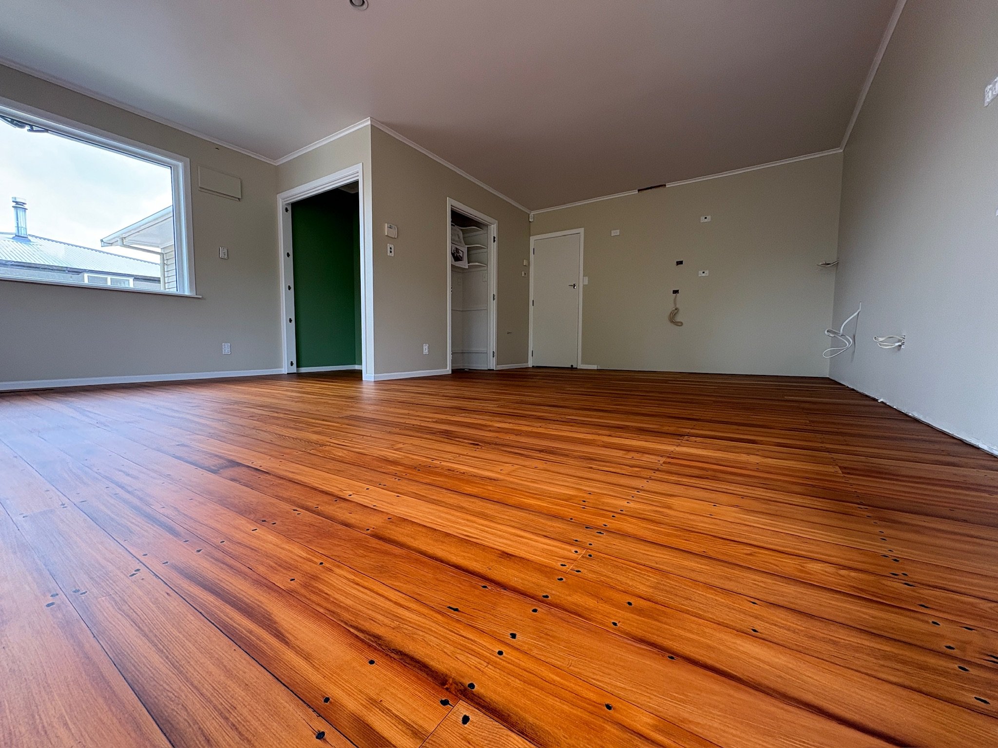 Empty room with wood flooring, white walls, a large window, and some electrical wires on the wall.
